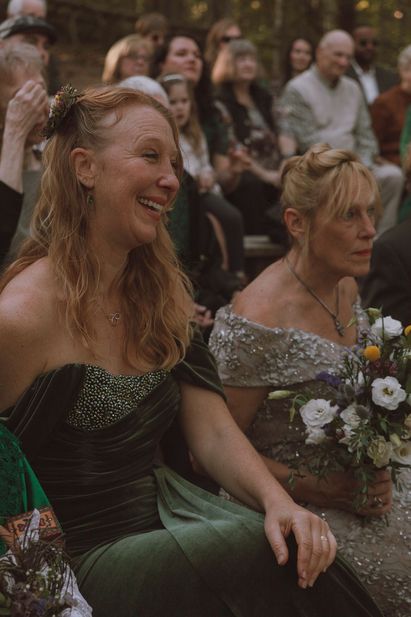 Wedding guests enjoy a candid moment at an outdoor celebration with a person in green velvet and another in sparkly attire.