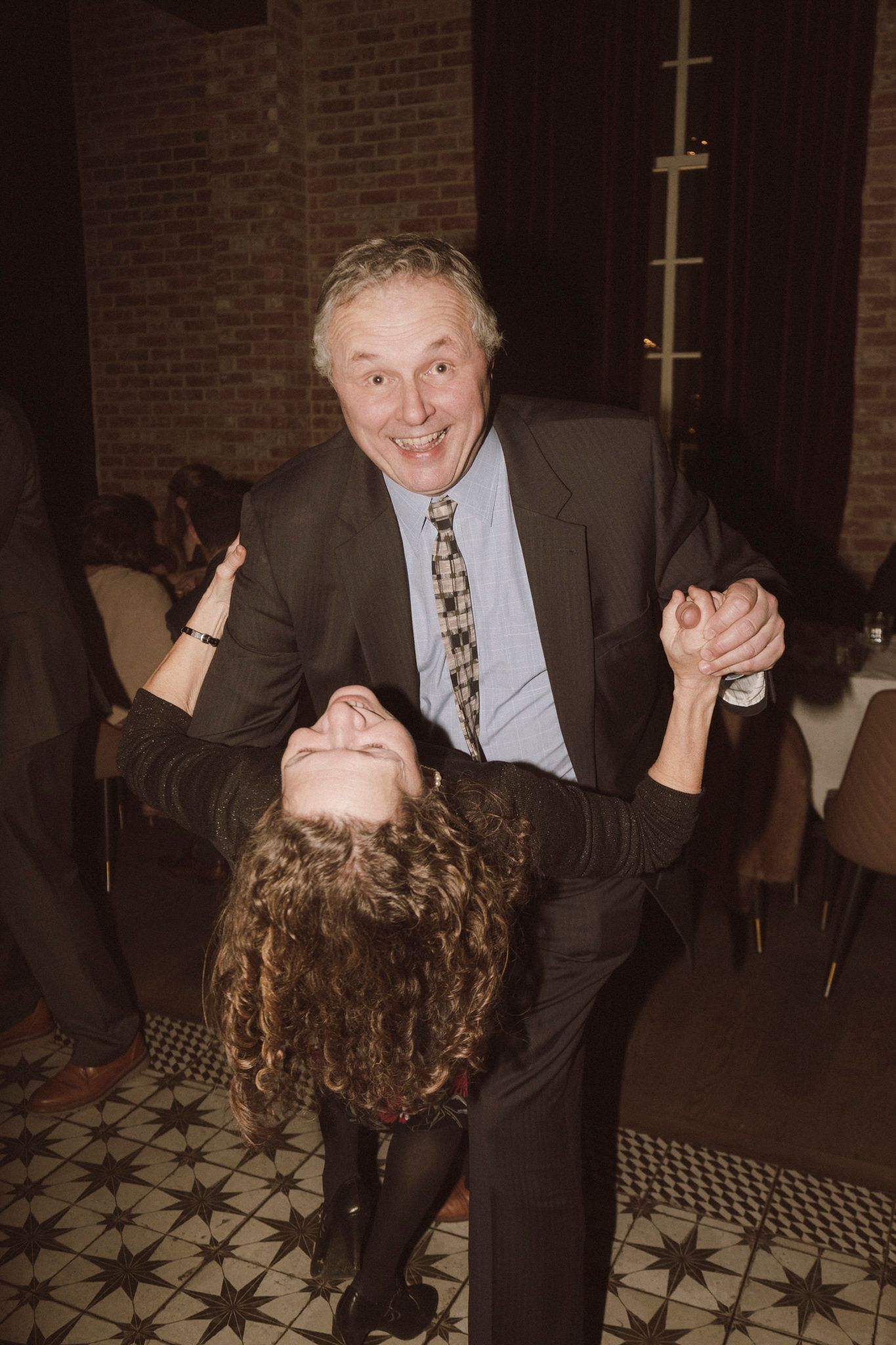 Elderly man in suit and tie dancing with young girl, dipping her at a wedding reception venue.