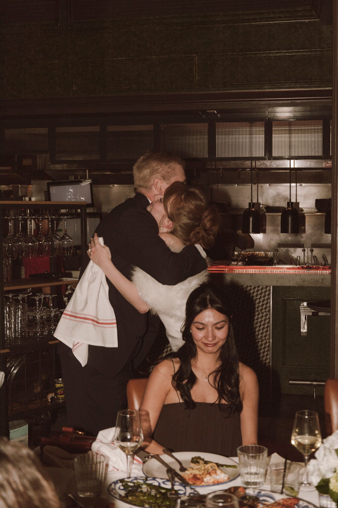 Bride and groom share a warm embrace near the kitchen at their intimate wedding reception dinner.