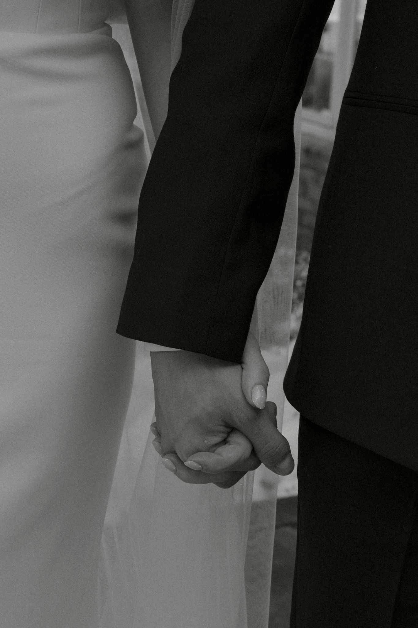 Black and white close-up of bride and groom holding hands, wedding attire visible.