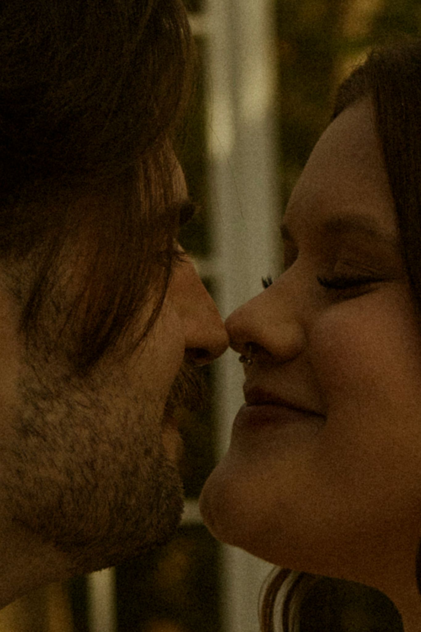Close-up of a couple sharing an intimate moment, nearly kissing, with warm tones highlighting their smiling faces.