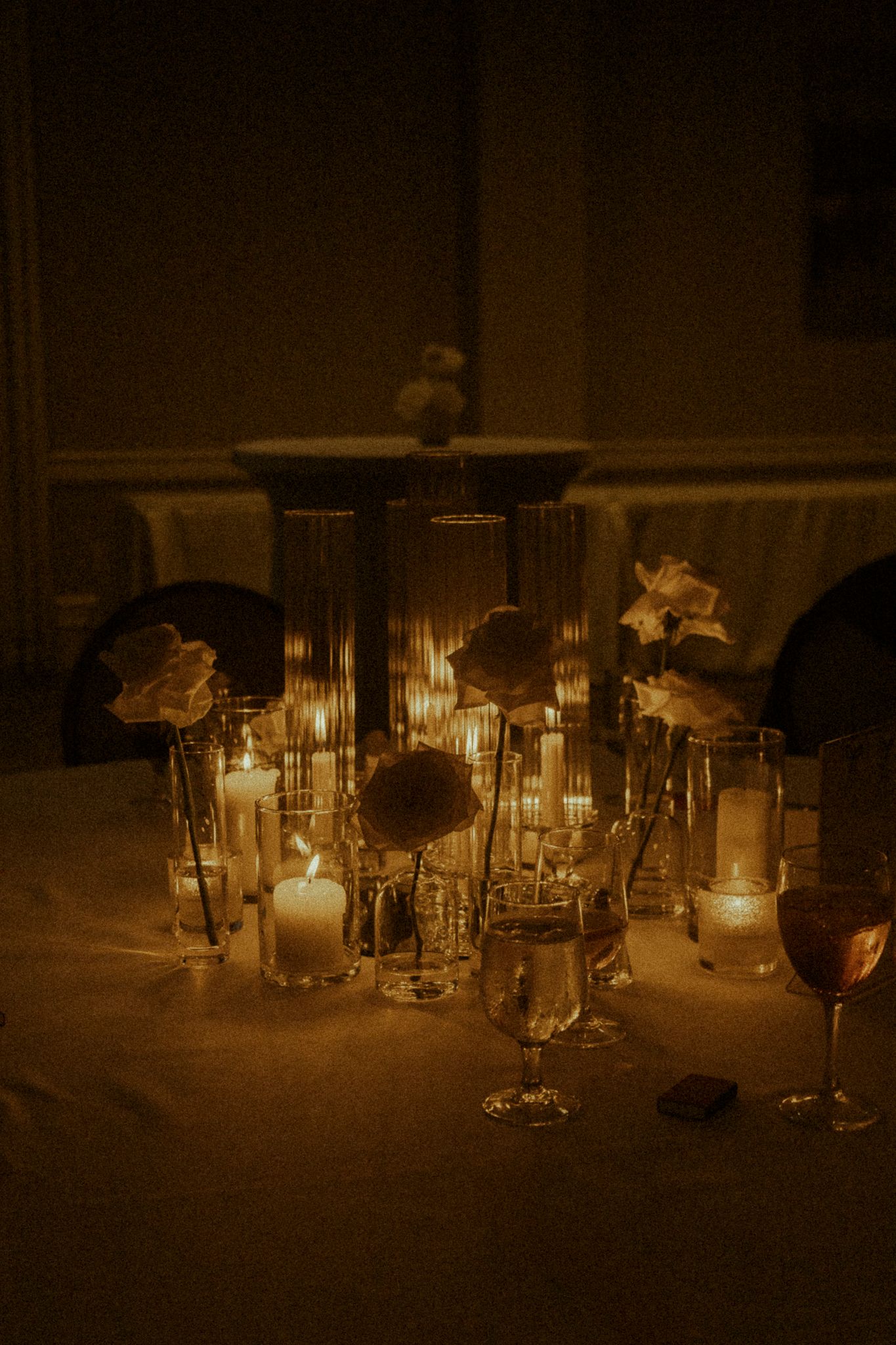 Romantic candlelit table centerpiece with roses, glass vases, and glowing candles creating warm ambiance for an elegant event.