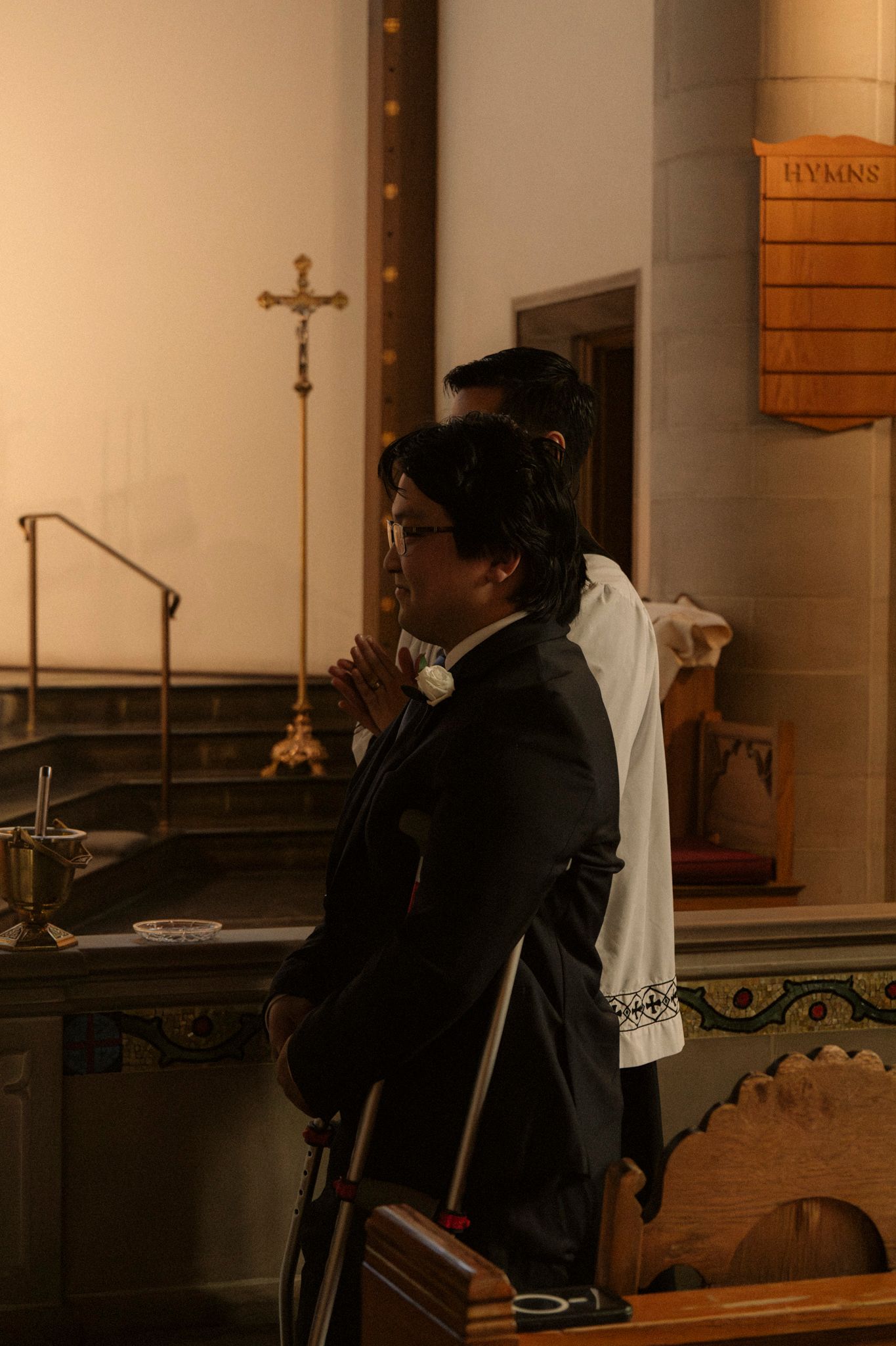Groom in black suit praying at church altar during Catholic wedding ceremony.