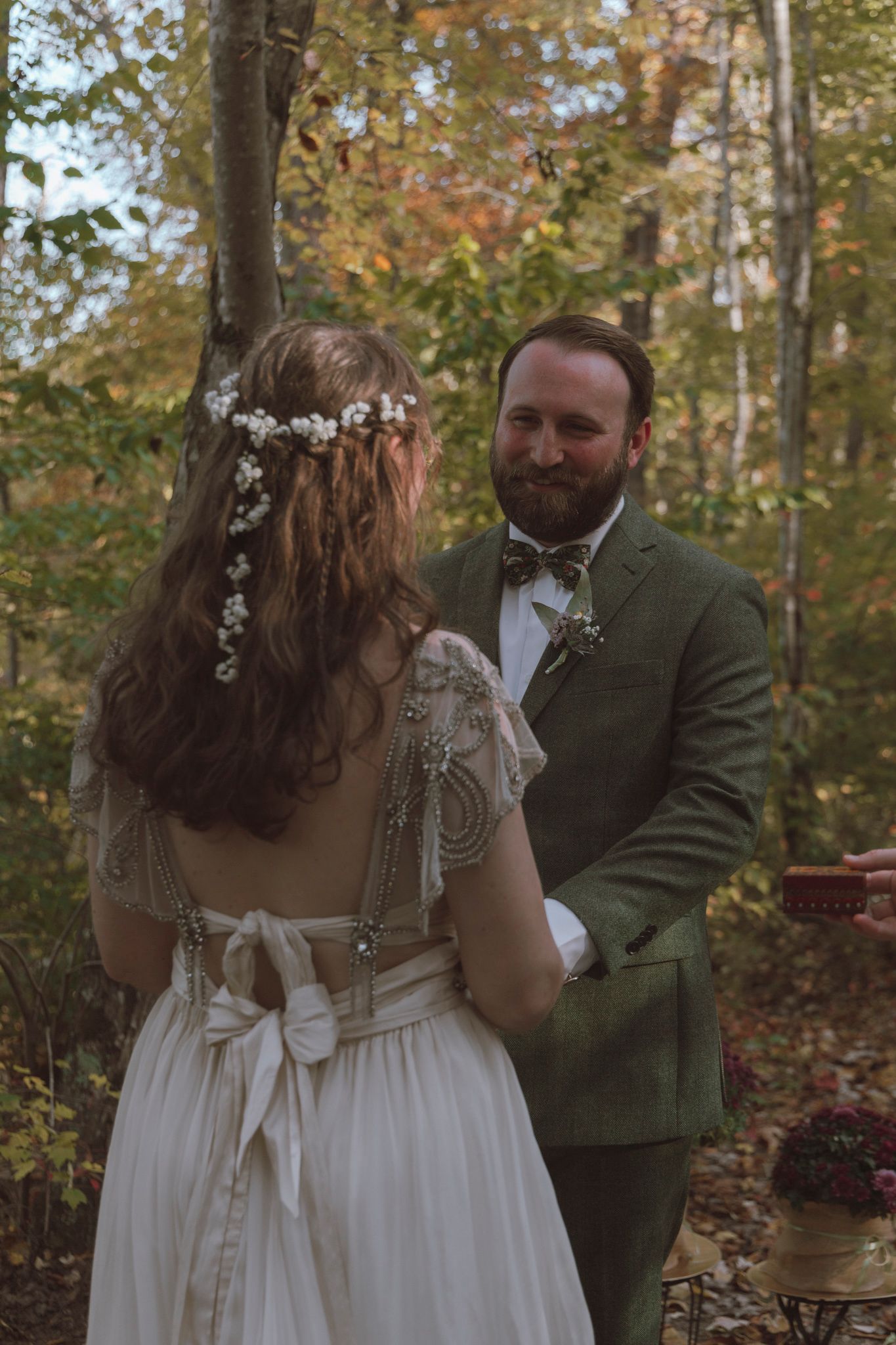 A couple in wedding attire embraces in an autumn forest setting with warm golden light filtering through the trees.