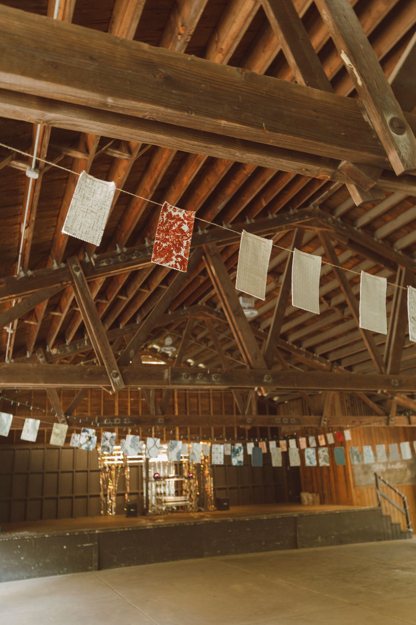 Interior of rustic wooden barn with exposed ceiling beams and decorative banners strung across the empty event space.