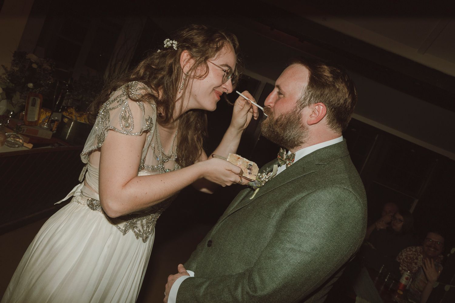 Newlywed couple sharing a playful moment while feeding each other cake at their wedding reception.