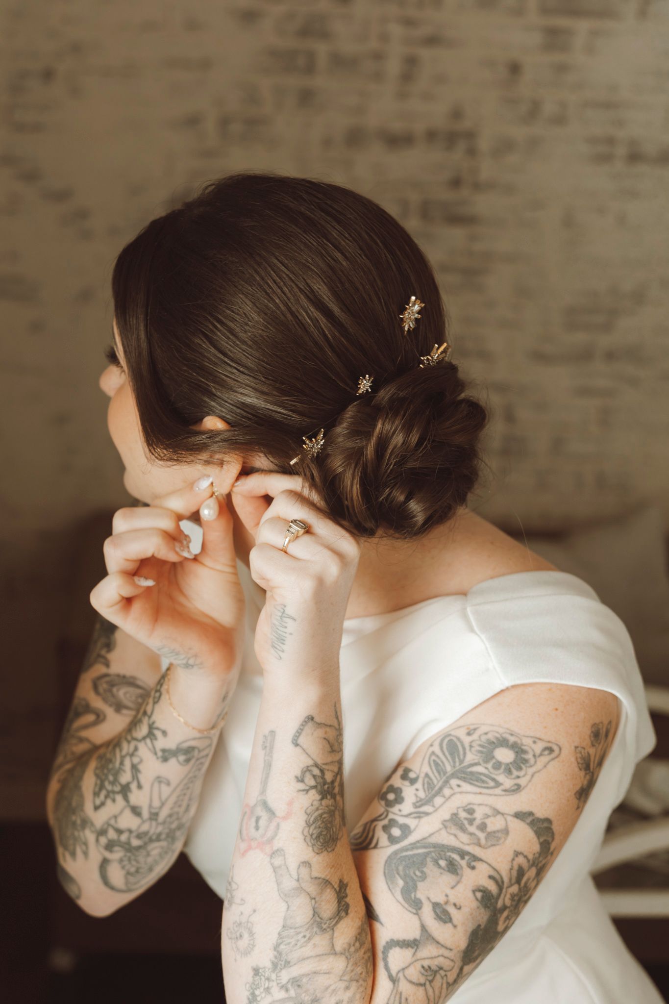 Close-up of tattooed arms and shoulders in white wedding dress during preparation.