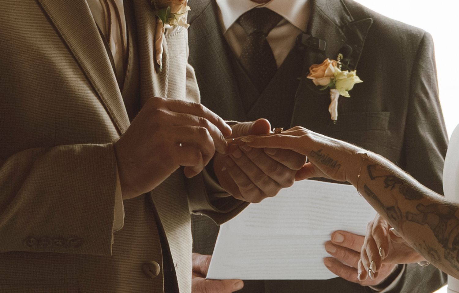 A series of hands shown in various positions signing wedding documents with a pen on white paper.