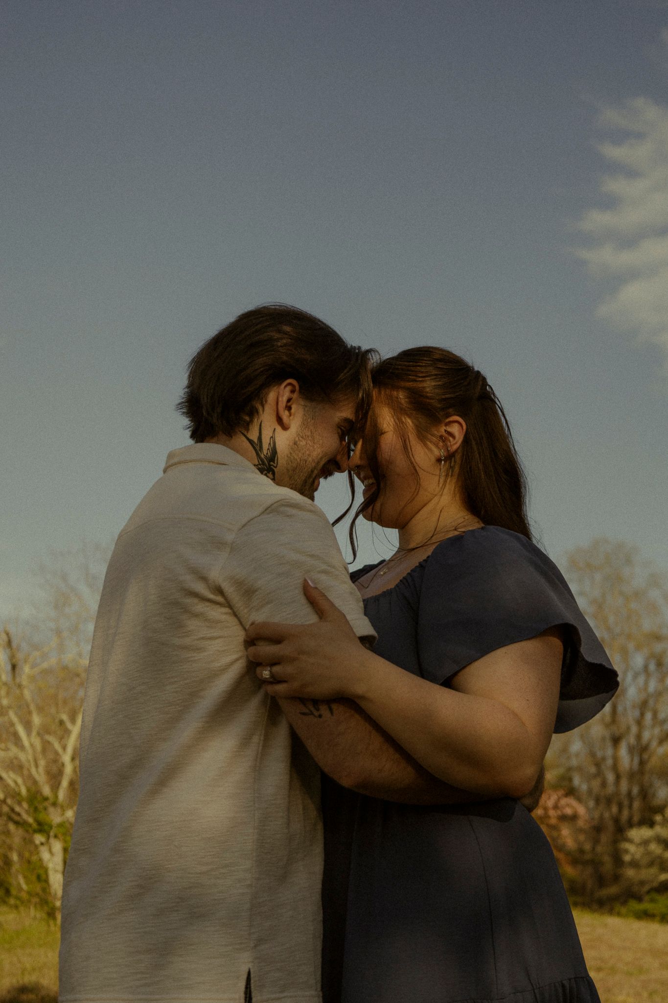 Couple sharing an intimate forehead-to-forehead moment outdoors under a blue sky.