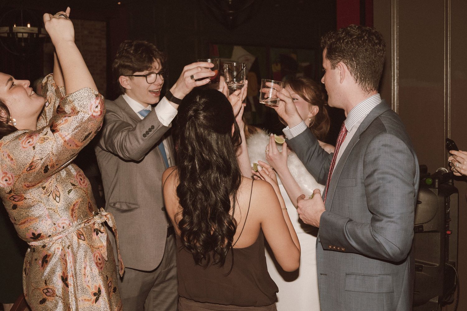 Wedding guests raising champagne glasses in celebratory toast at lively reception party.