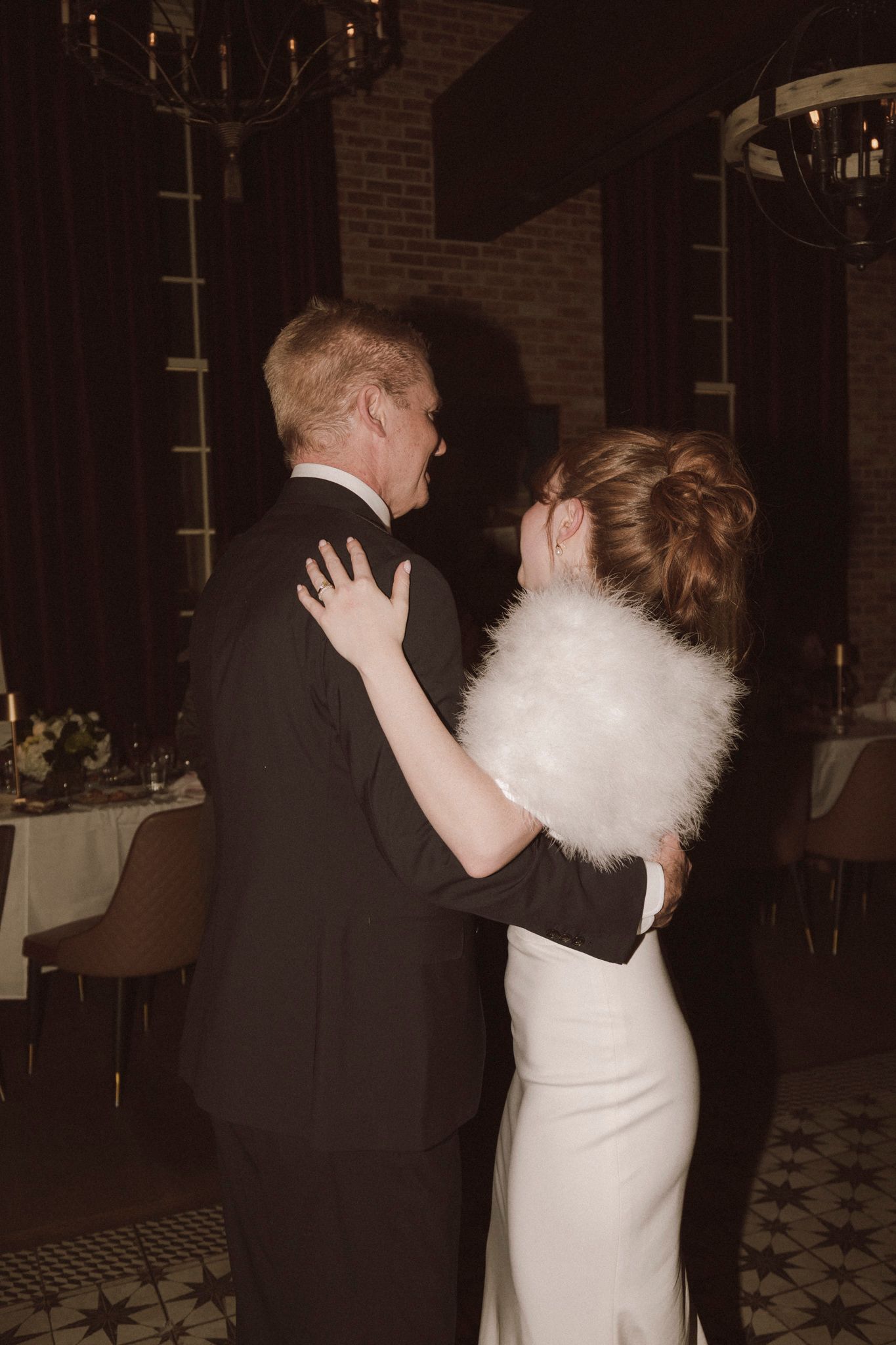 Bride and groom sharing first dance, bride wearing white gown with fur stole.