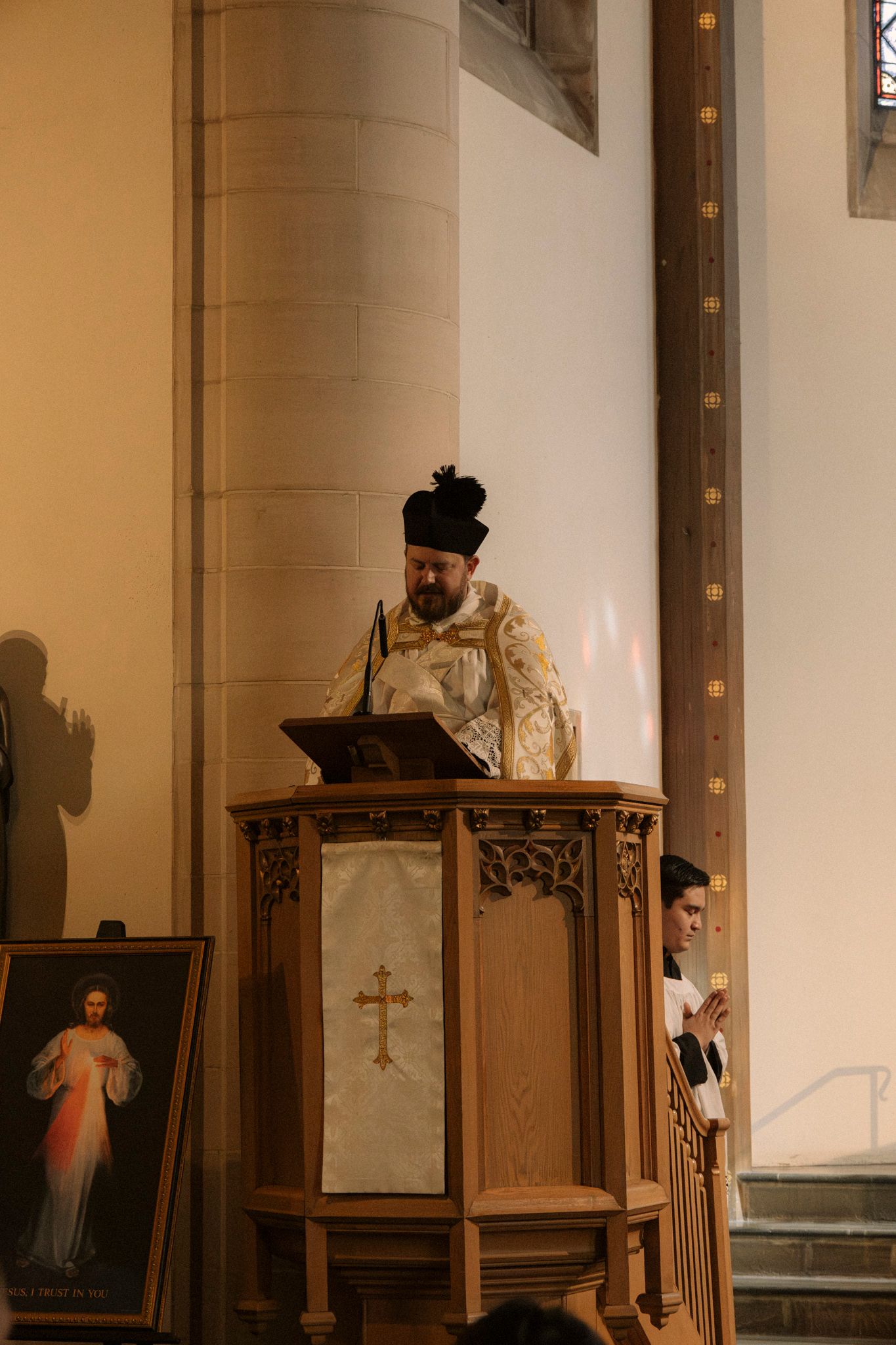 Catholic priest in gold vestments delivers sermon at ornate wooden pulpit during wedding Mass.