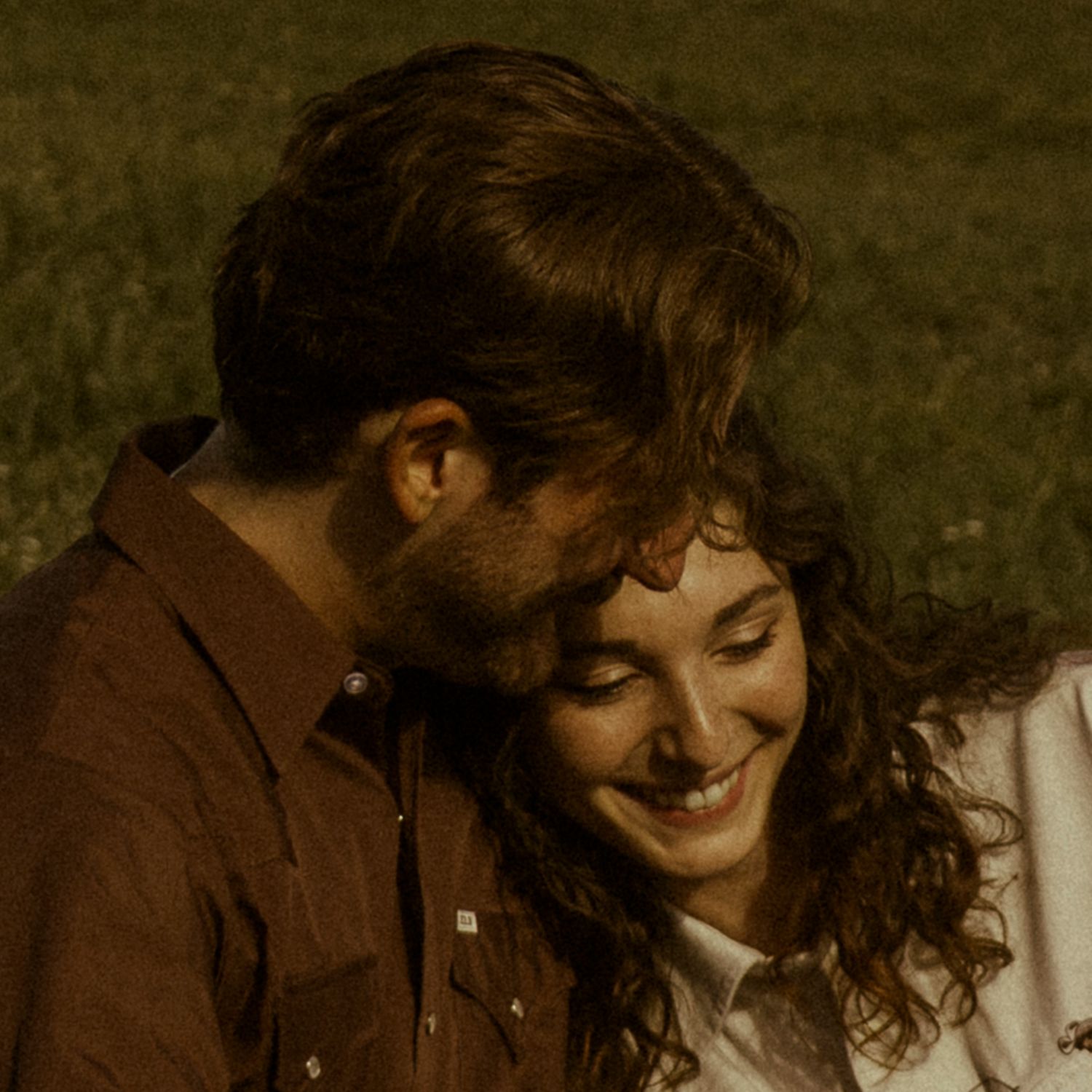 A couple shares a tender moment outdoors at dusk, the woman smiling warmly as she leans against the man.