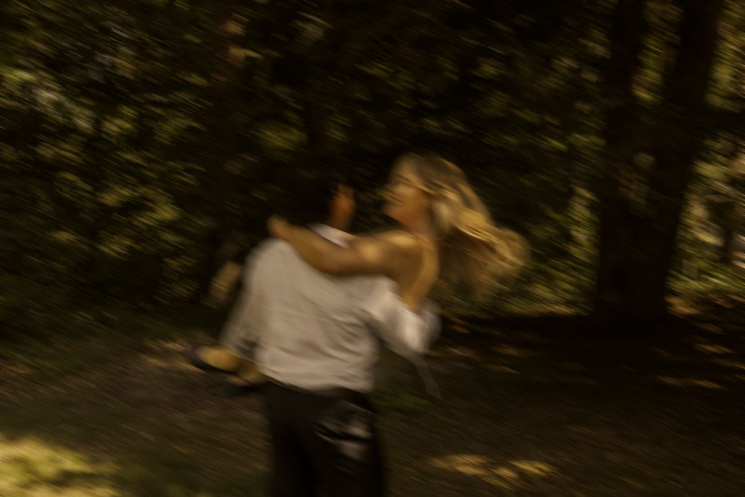 Blurry motion shot of a couple embracing and dancing together in a sunlit forest setting.
