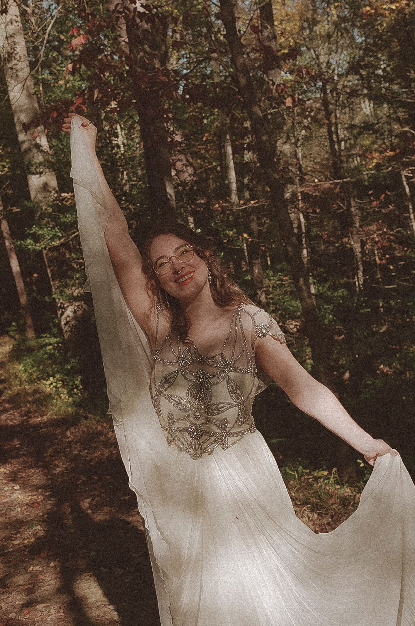 A person in a flowing white wedding dress twirls joyfully in a sunlit autumn forest setting.