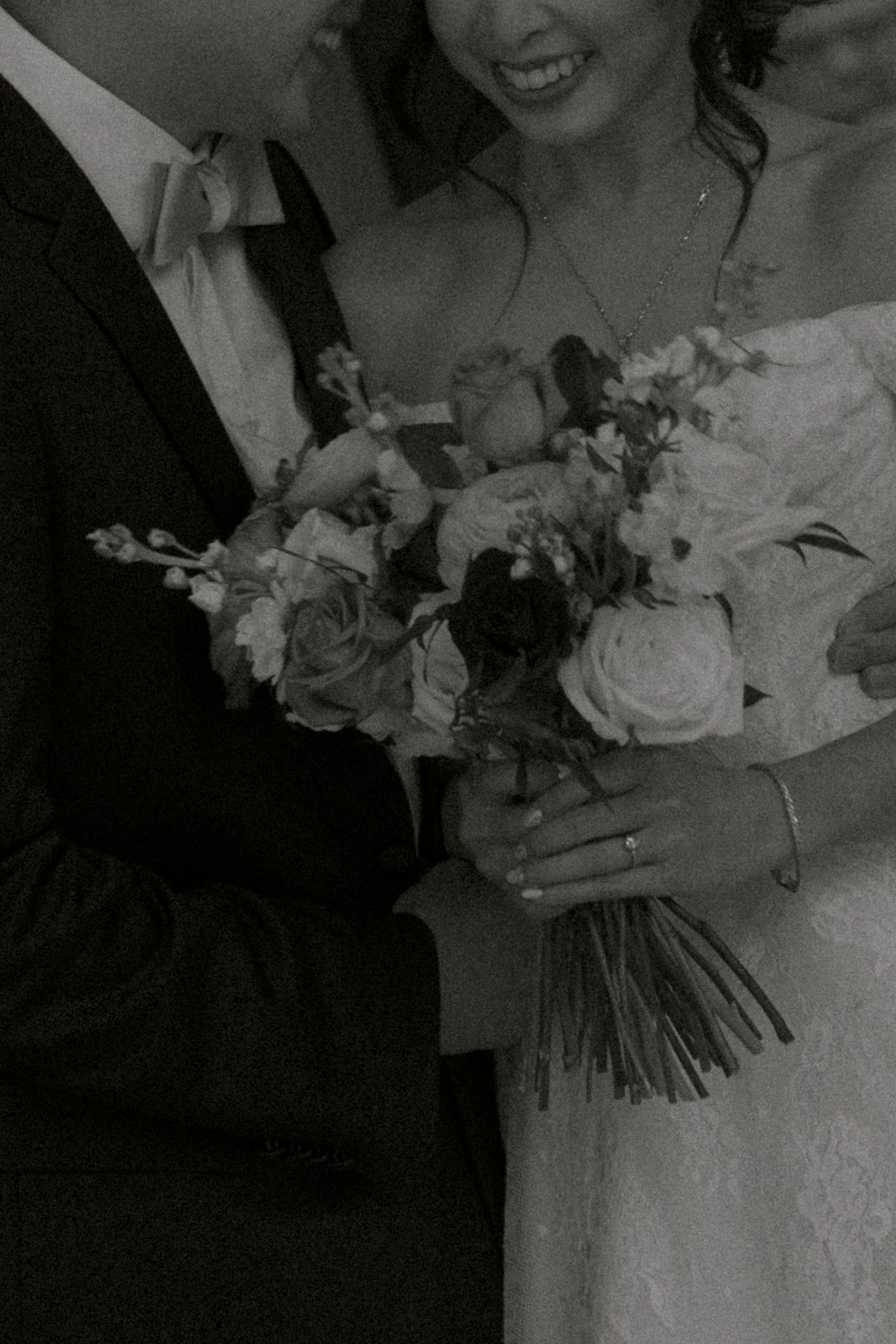 Black and white wedding photo showing couple holding elegant bouquet of roses and mixed flowers.