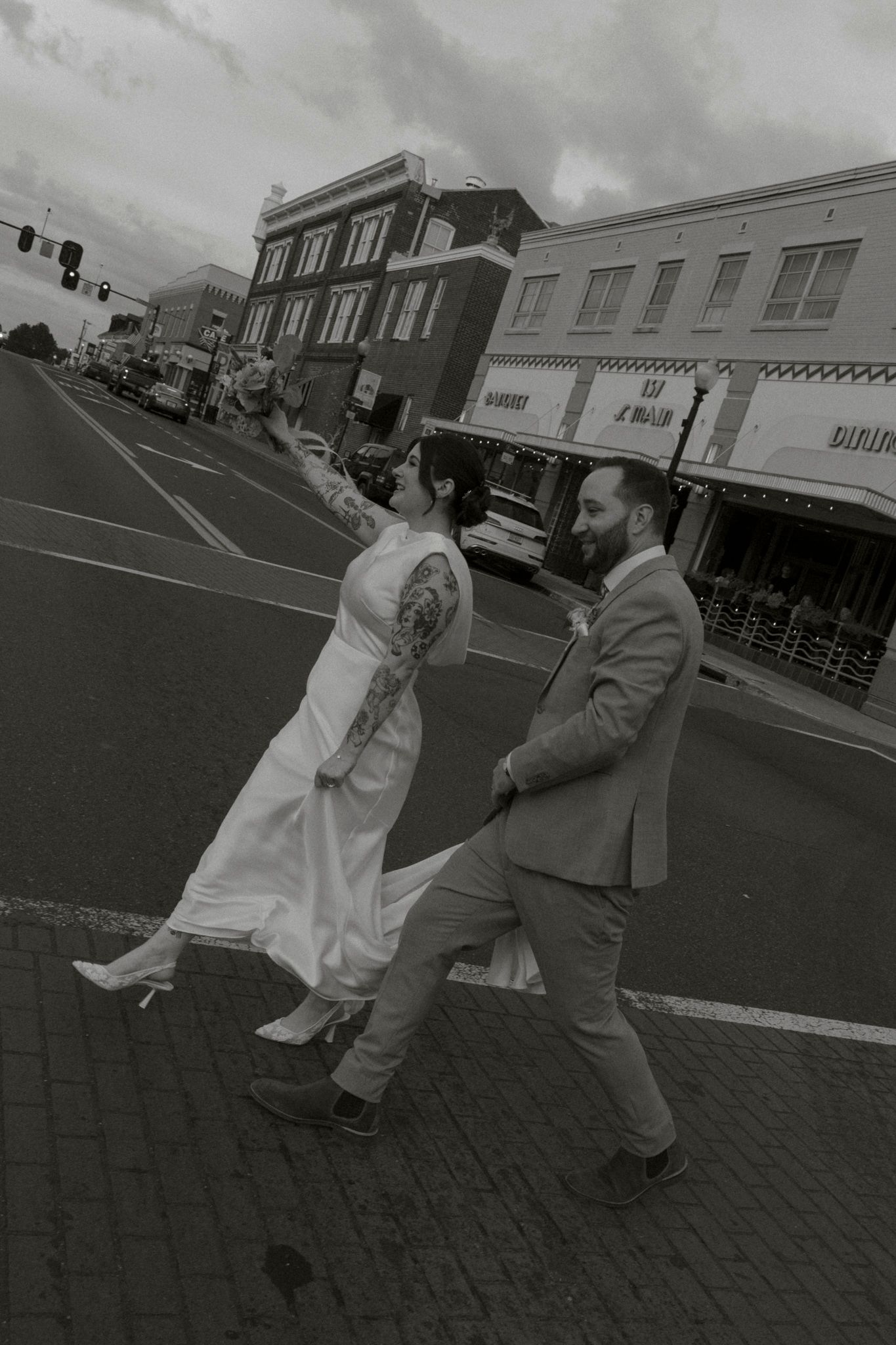 Playful dance sequence of a wedding couple on a brick street in black and white.