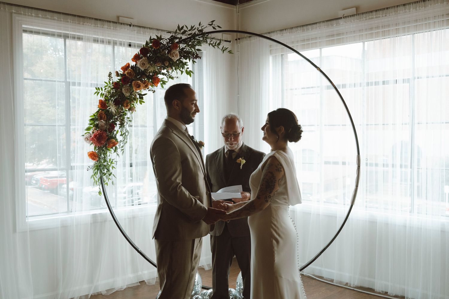 Wedding guests mingling in a light-filled room decorated with hanging floral arrangements.