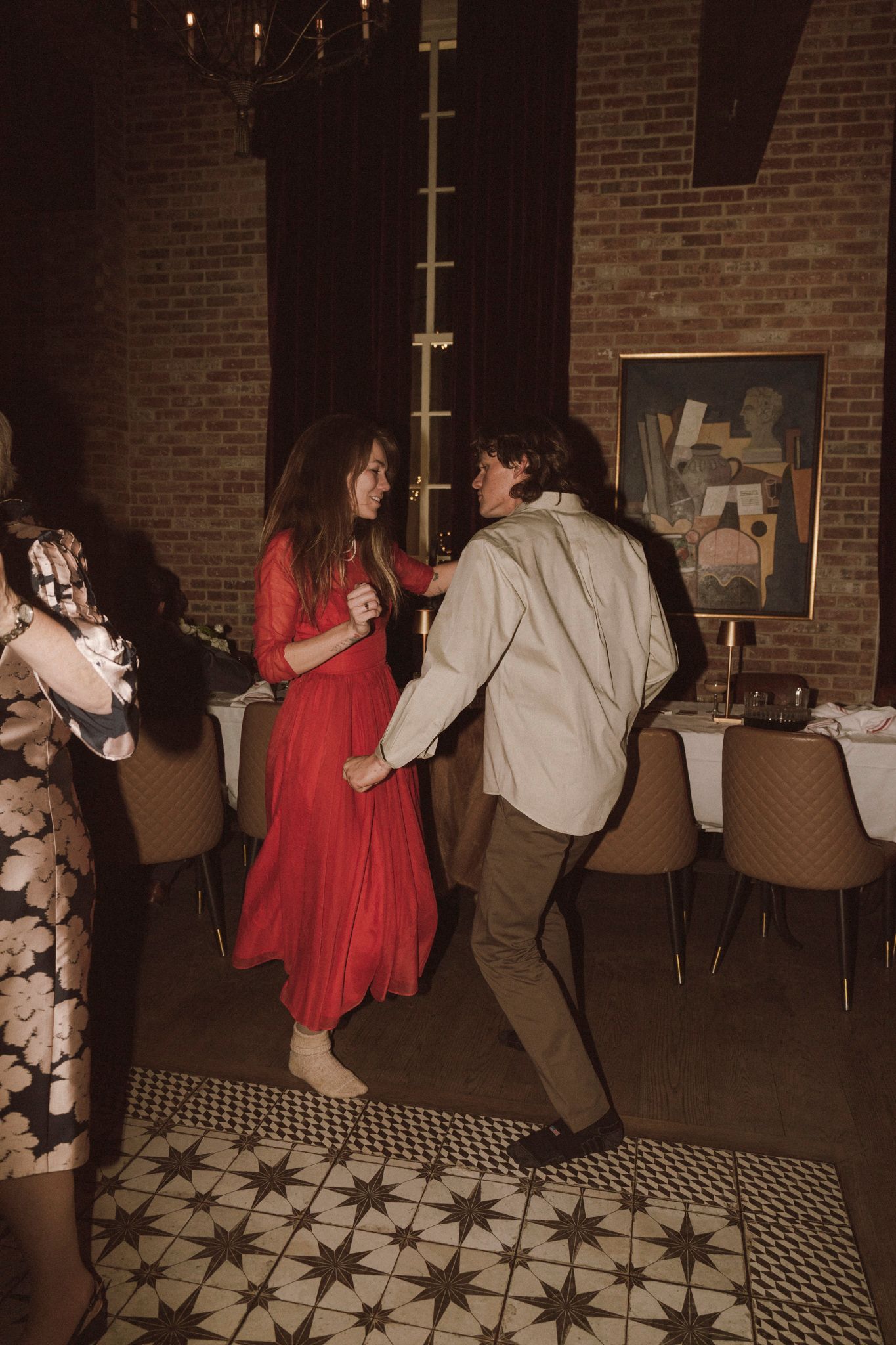 Woman in red dress dances energetically with man in white shirt at lively wedding reception.