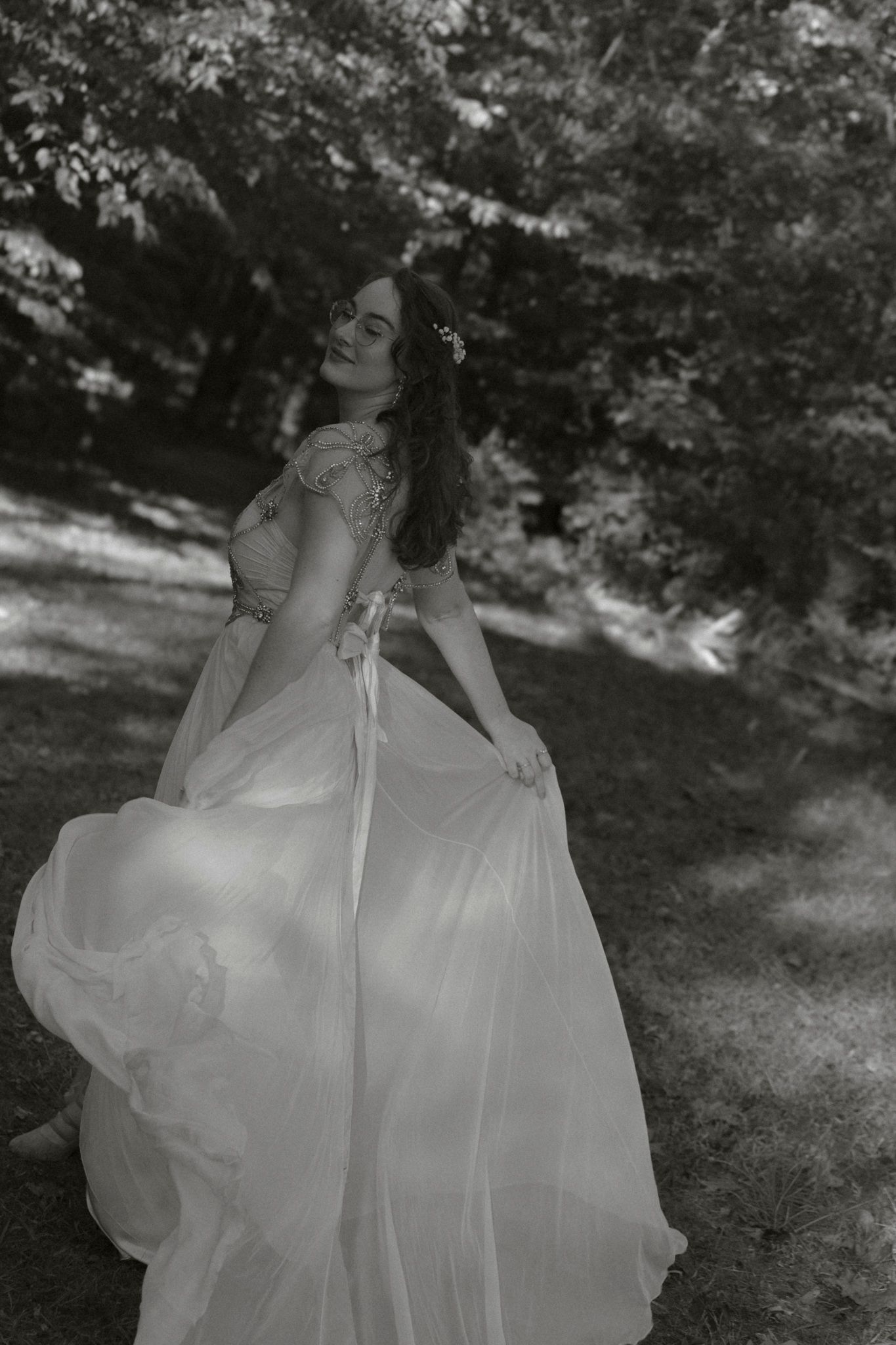 A flowing white wedding dress billows gracefully in the breeze as someone twirls in a sunlit garden setting.