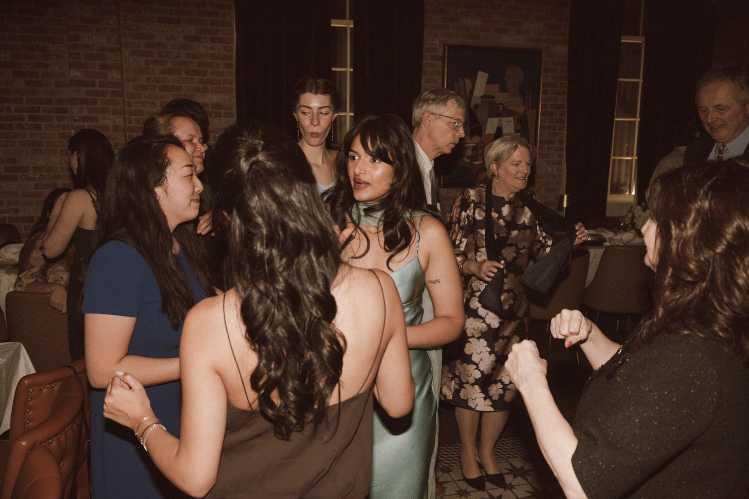 Wedding guests socializing at reception, woman in sage green dress at center of group.