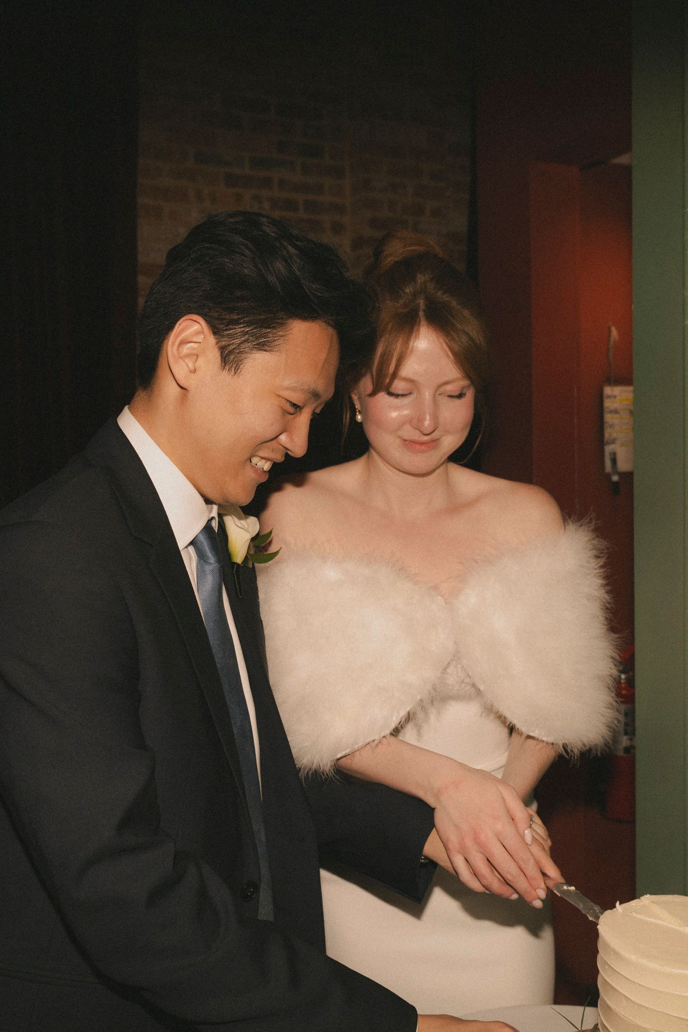 Bride and groom cutting their wedding cake, bride wearing white fur stole and groom in black suit.