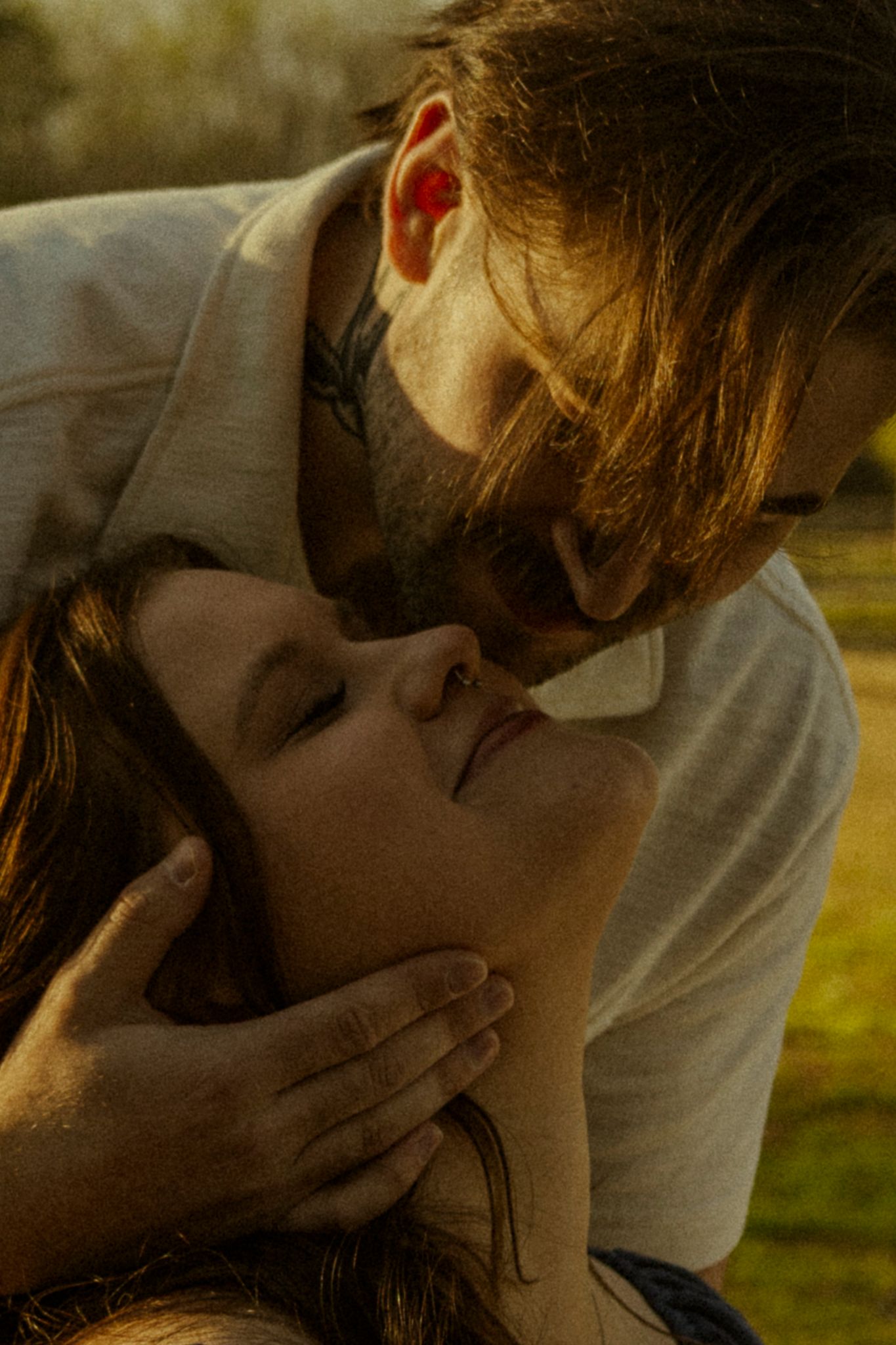 A couple shares an intimate moment outdoors, man gently holding womans face as they lean in close together.