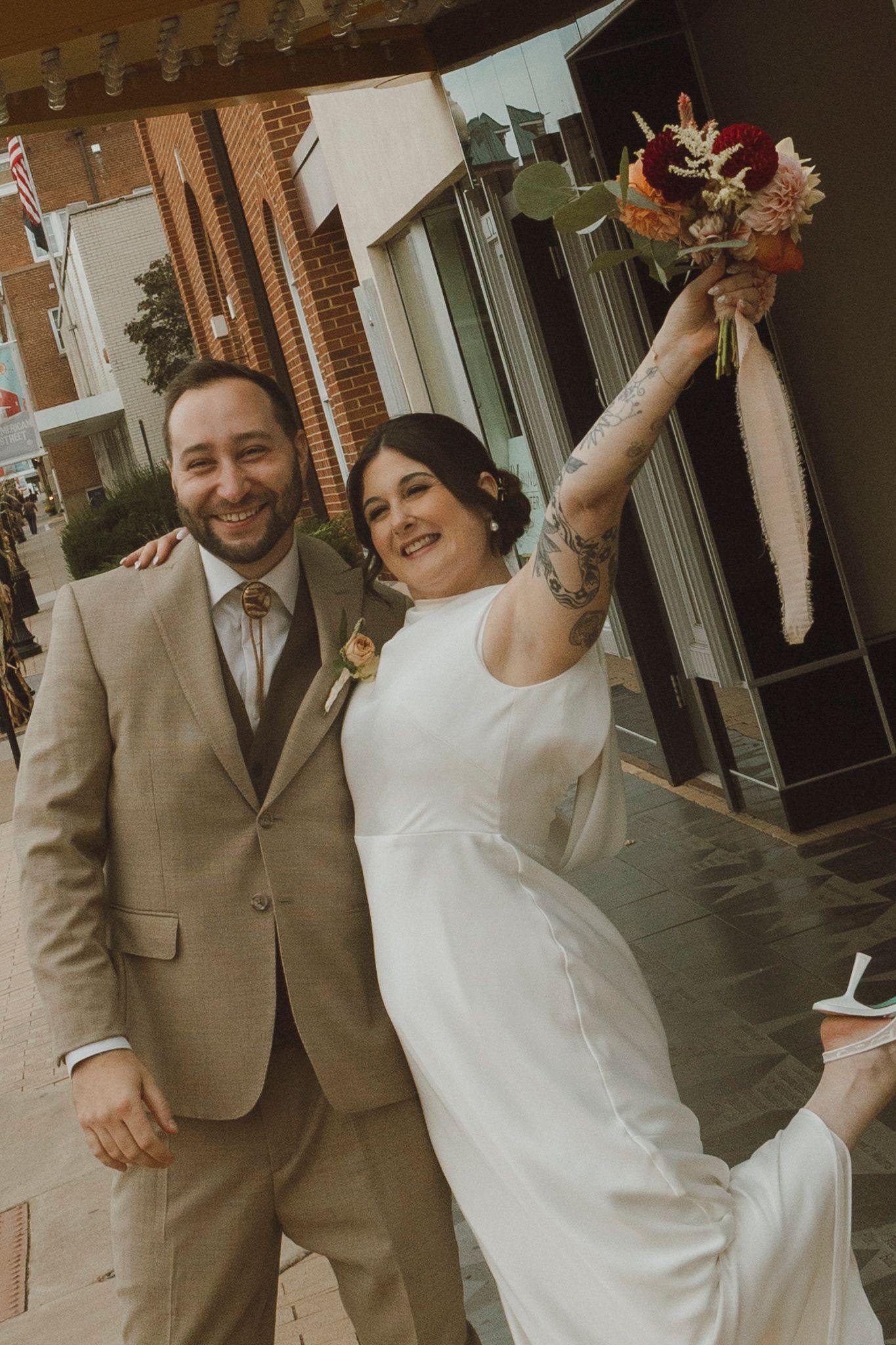 A celebratory wedding couple dances and laughs outside a historic theater.