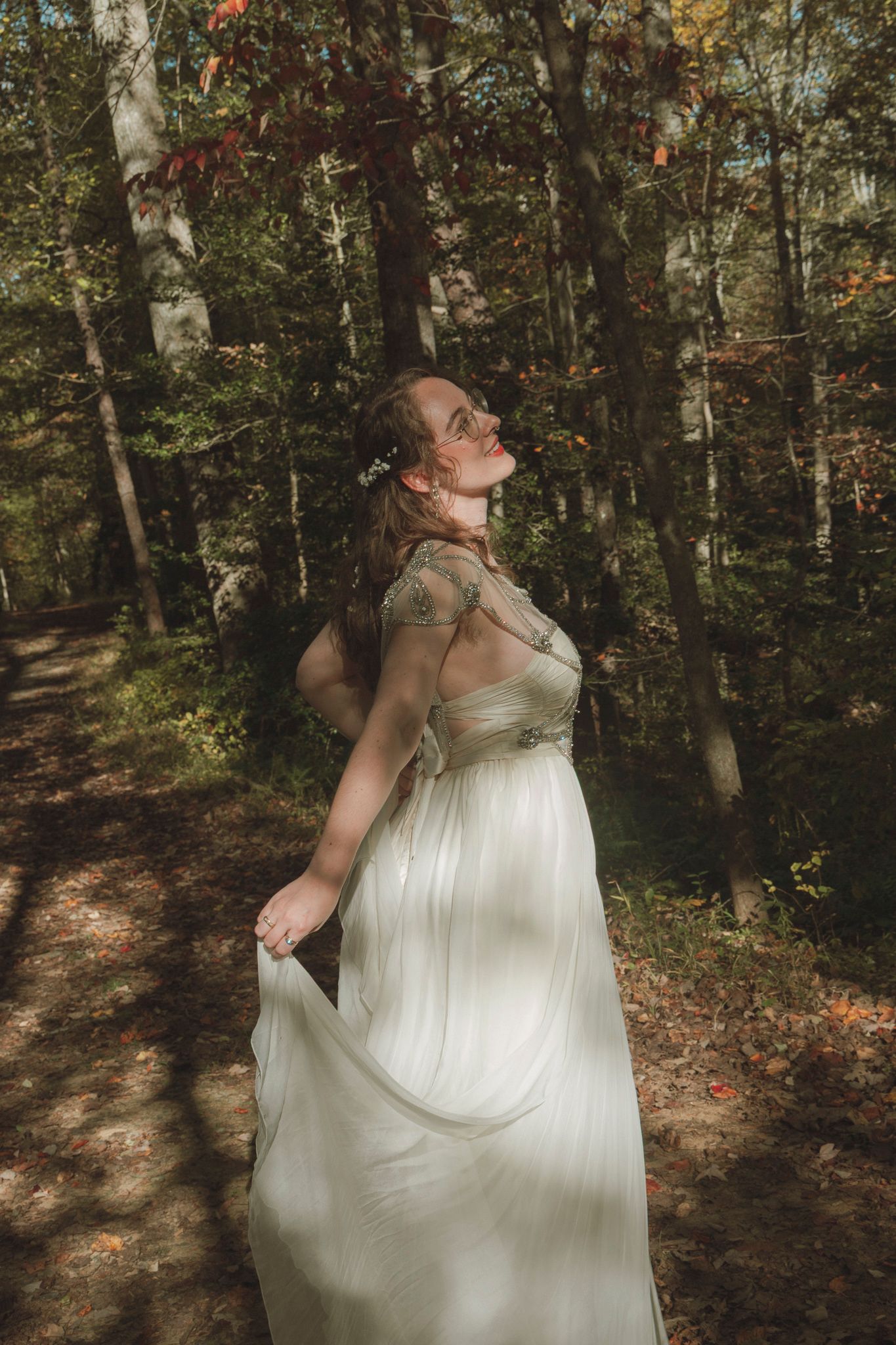 A flowing white dress catches sunlight in a forest setting as the wearer tilts back in an ethereal pose.