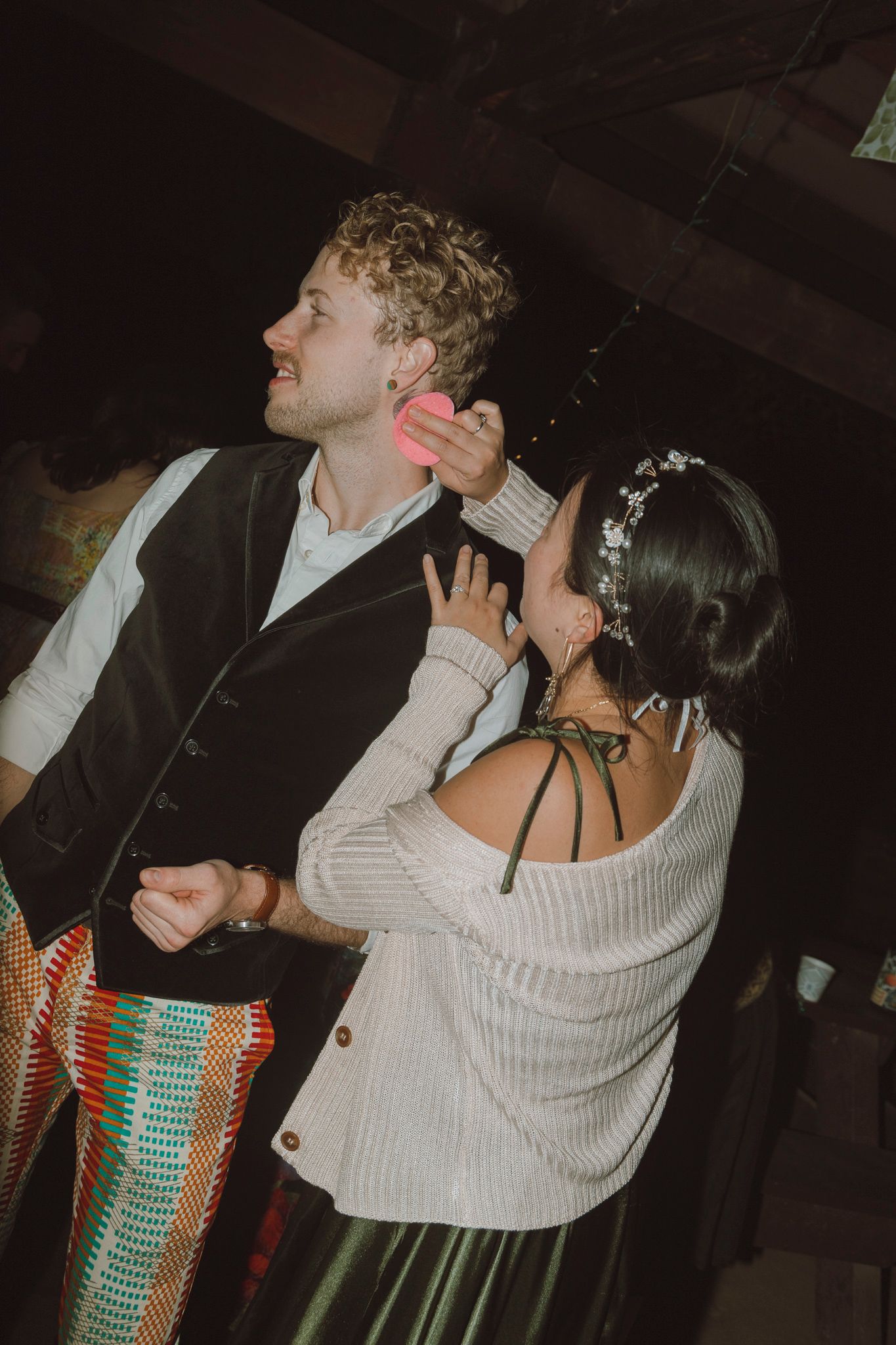 Two people dance together in an intimate embrace under dim lighting at what appears to be a party or event.