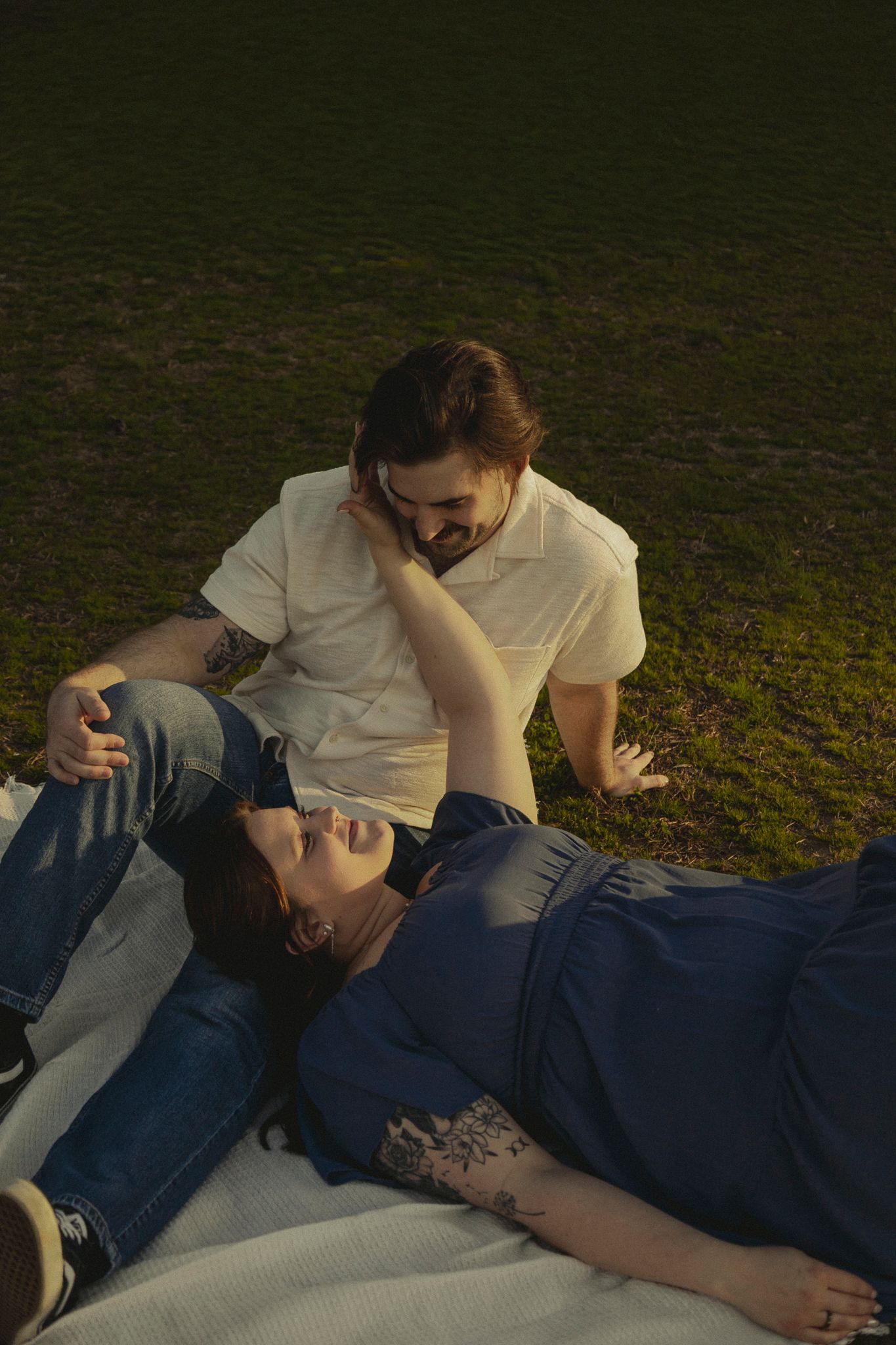 Couple sharing a tender moment on a blanket in the grass during a sunny outdoor picnic.