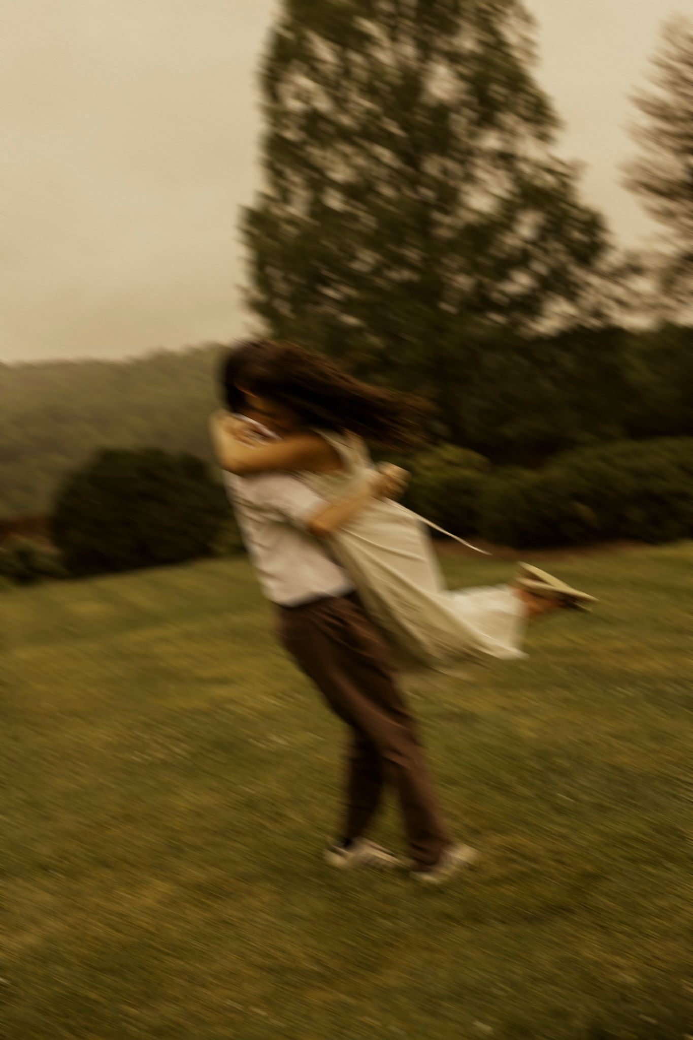 A couple embraces and spins joyfully in a lush green park, captured in a romantic motion-blurred photograph.