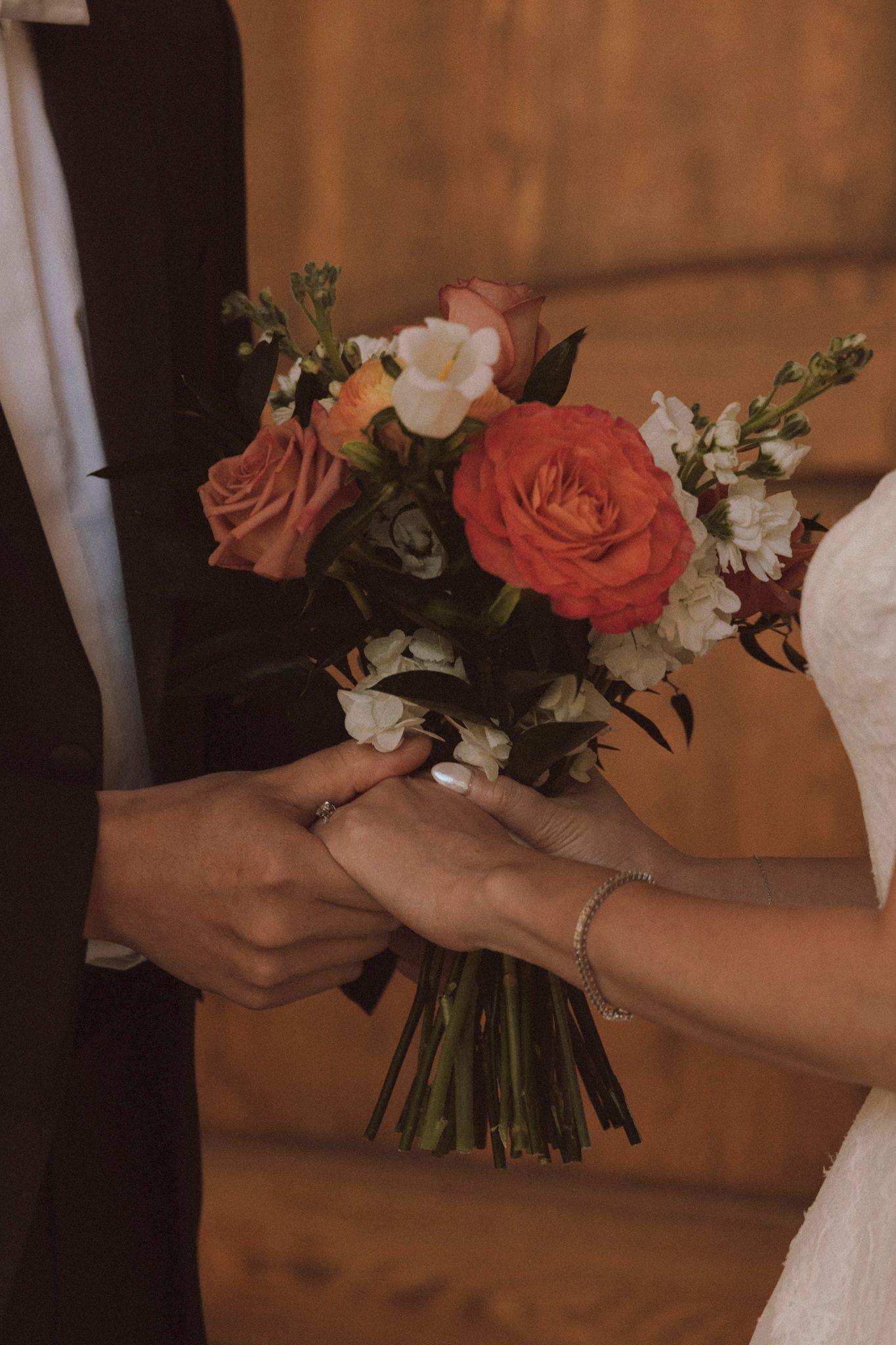 Close-up shot of hands holding a wedding bouquet with coral roses and white flowers.