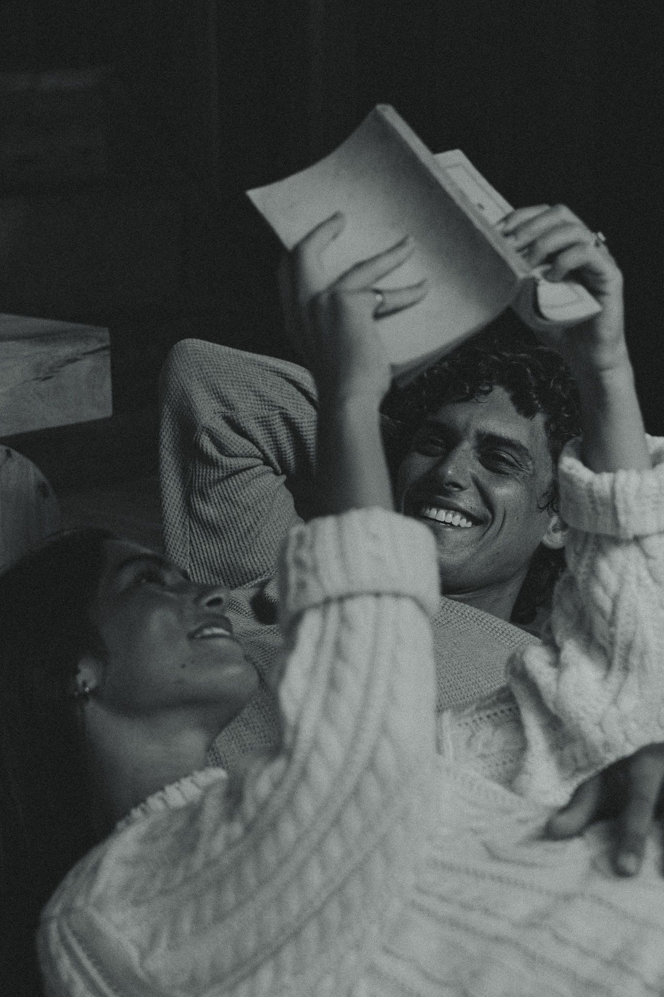 Black and white photo of a laughing couple lying down together, one holding a book above their heads.