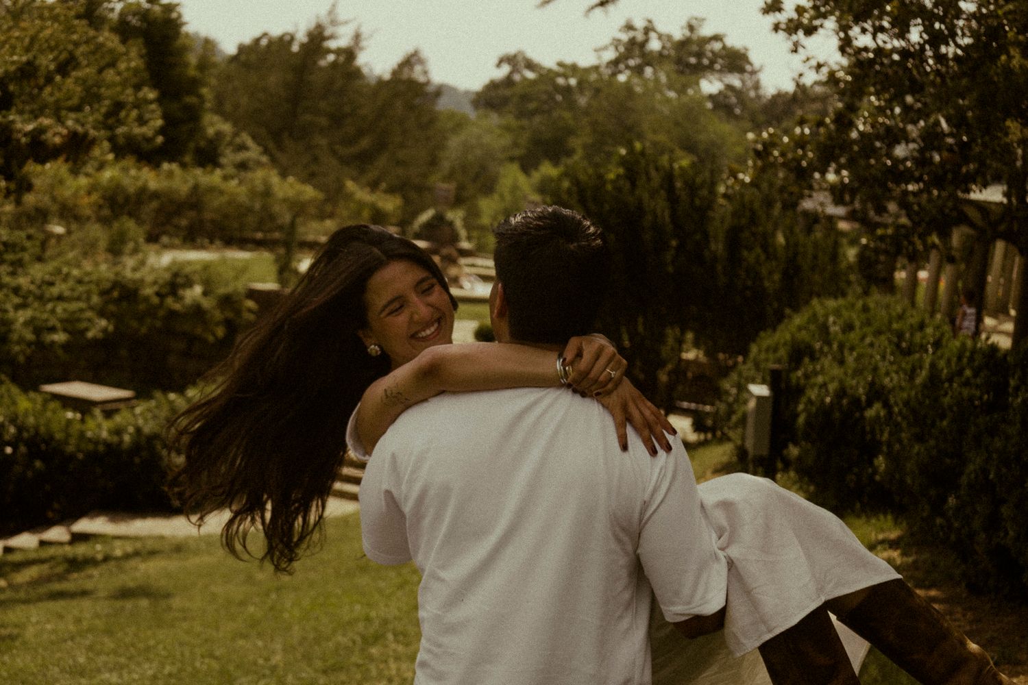 Couple embracing and spinning joyfully in a green outdoor garden setting.