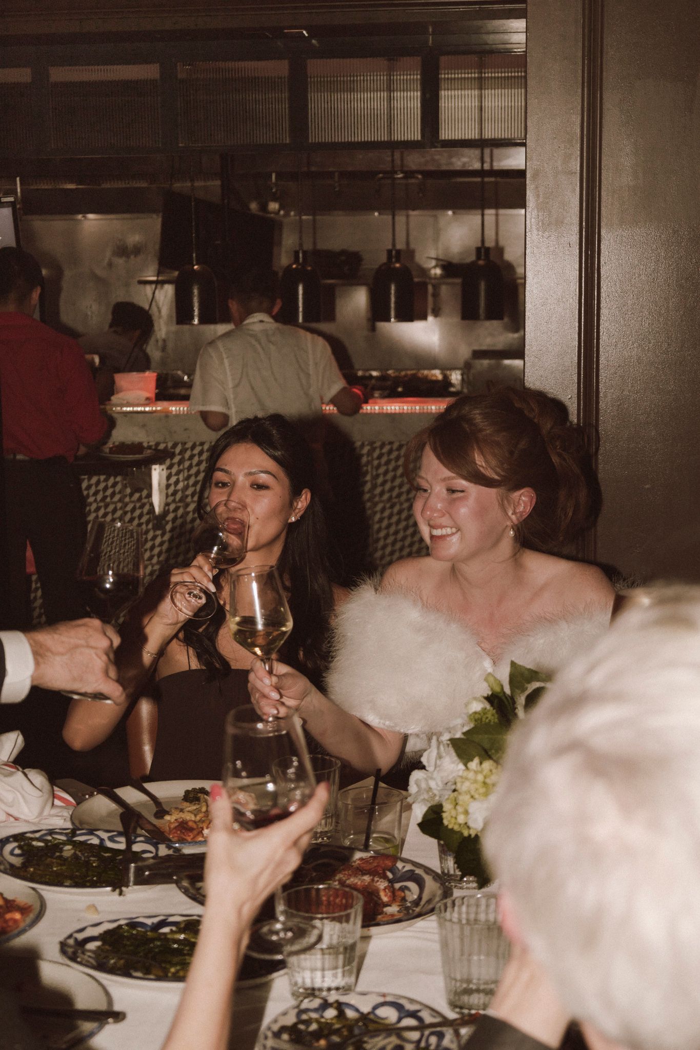 Bride in white fur stole toasting with wine glasses at elegant wedding reception dinner table.