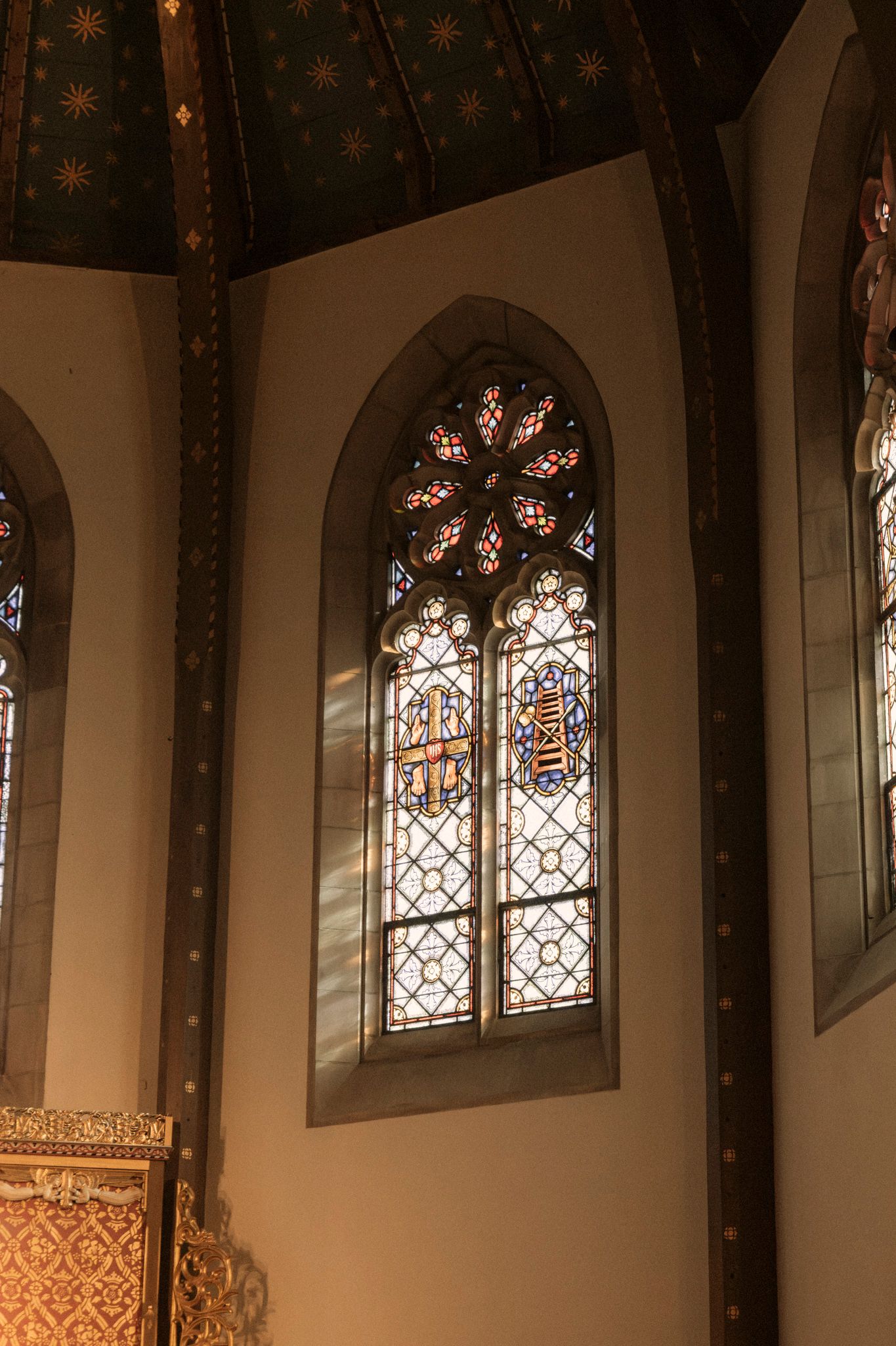 Ornate stained glass window with rose detail in an octagonal chapel with decorative painted ceiling.