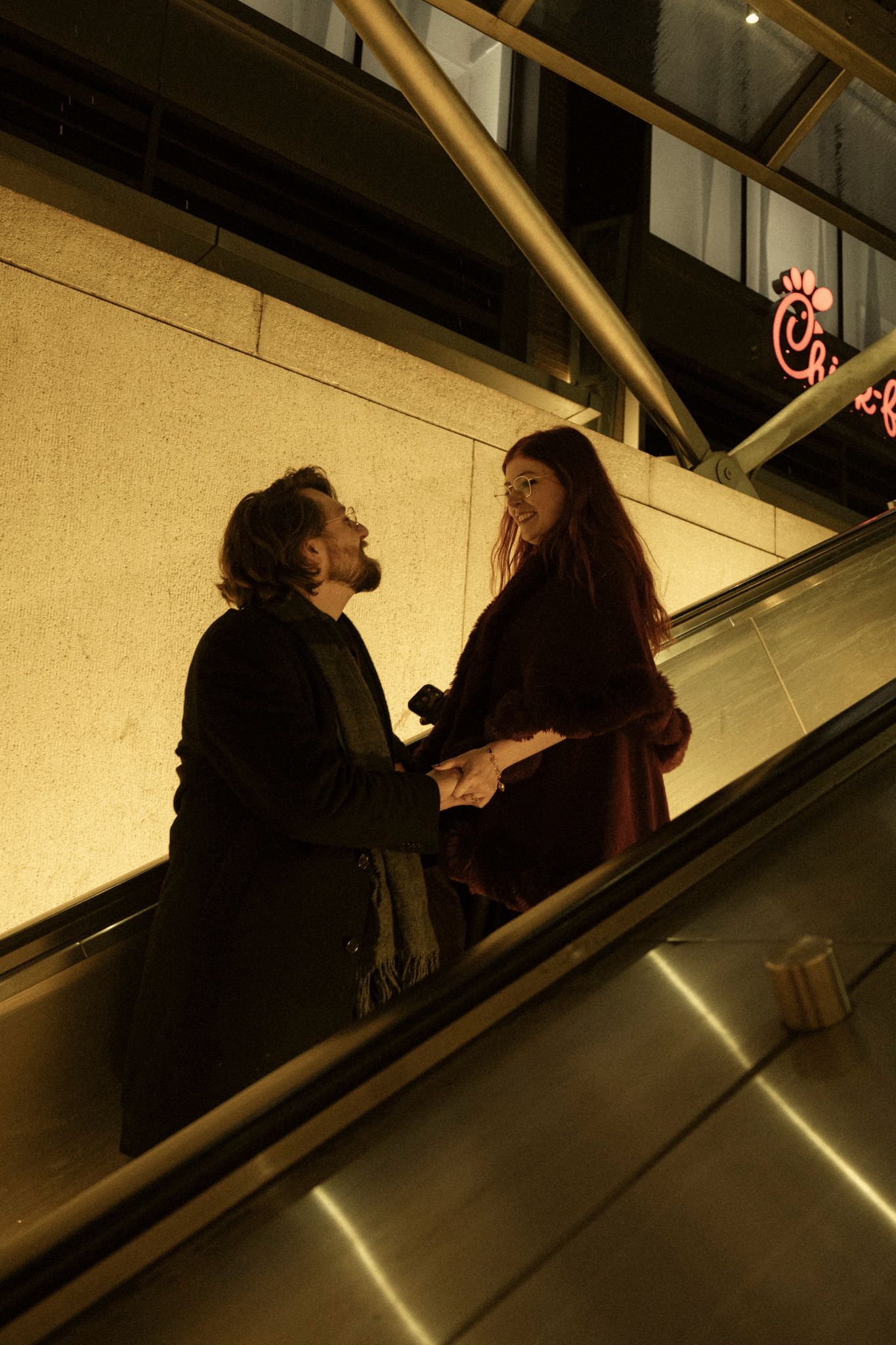 People riding an escalator in a dimly lit space with dramatic lighting and shadows.