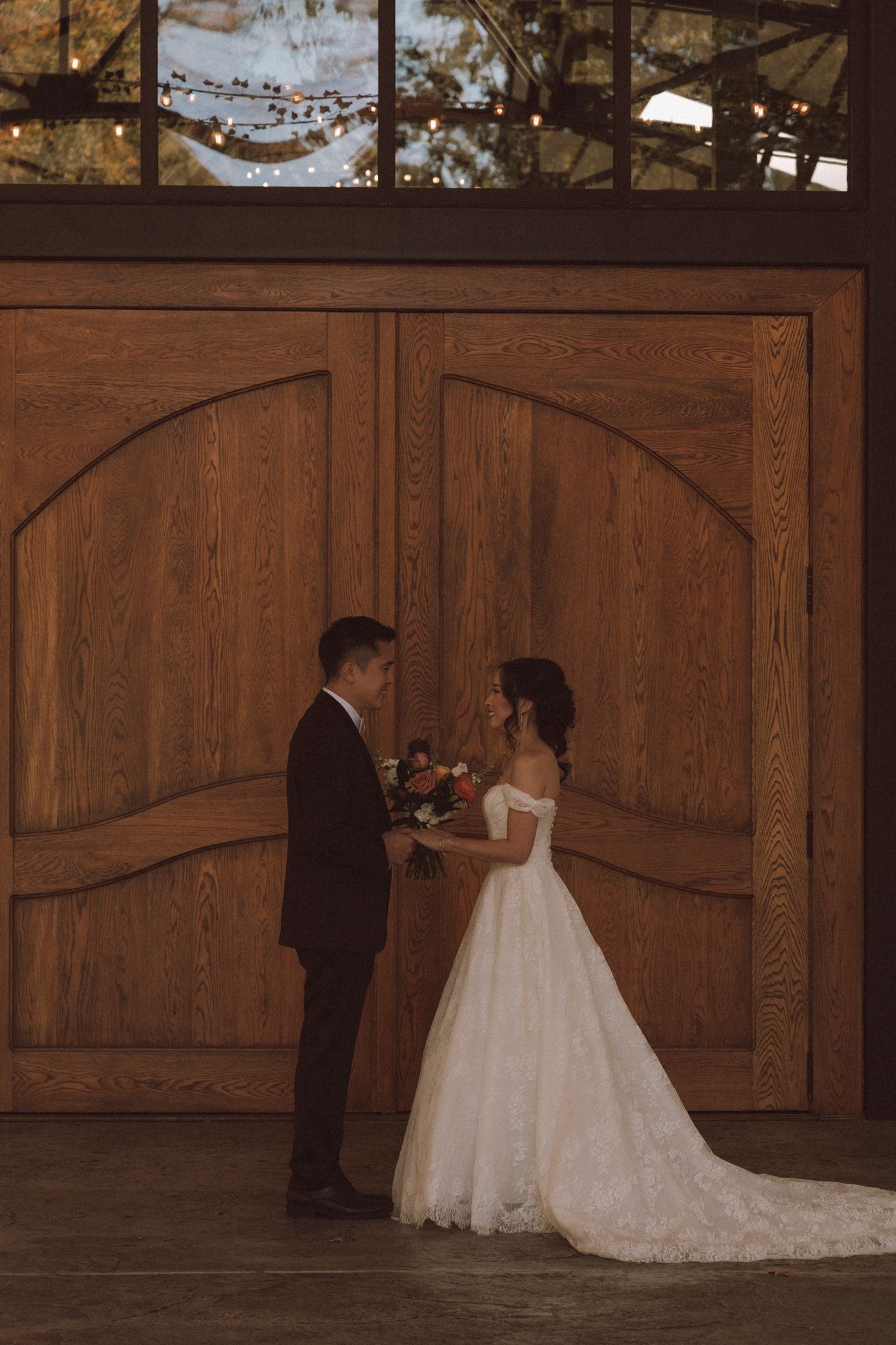 A first look sequence showing a couple in formal wedding attire meeting at a rustic wooden door in a barn setting.