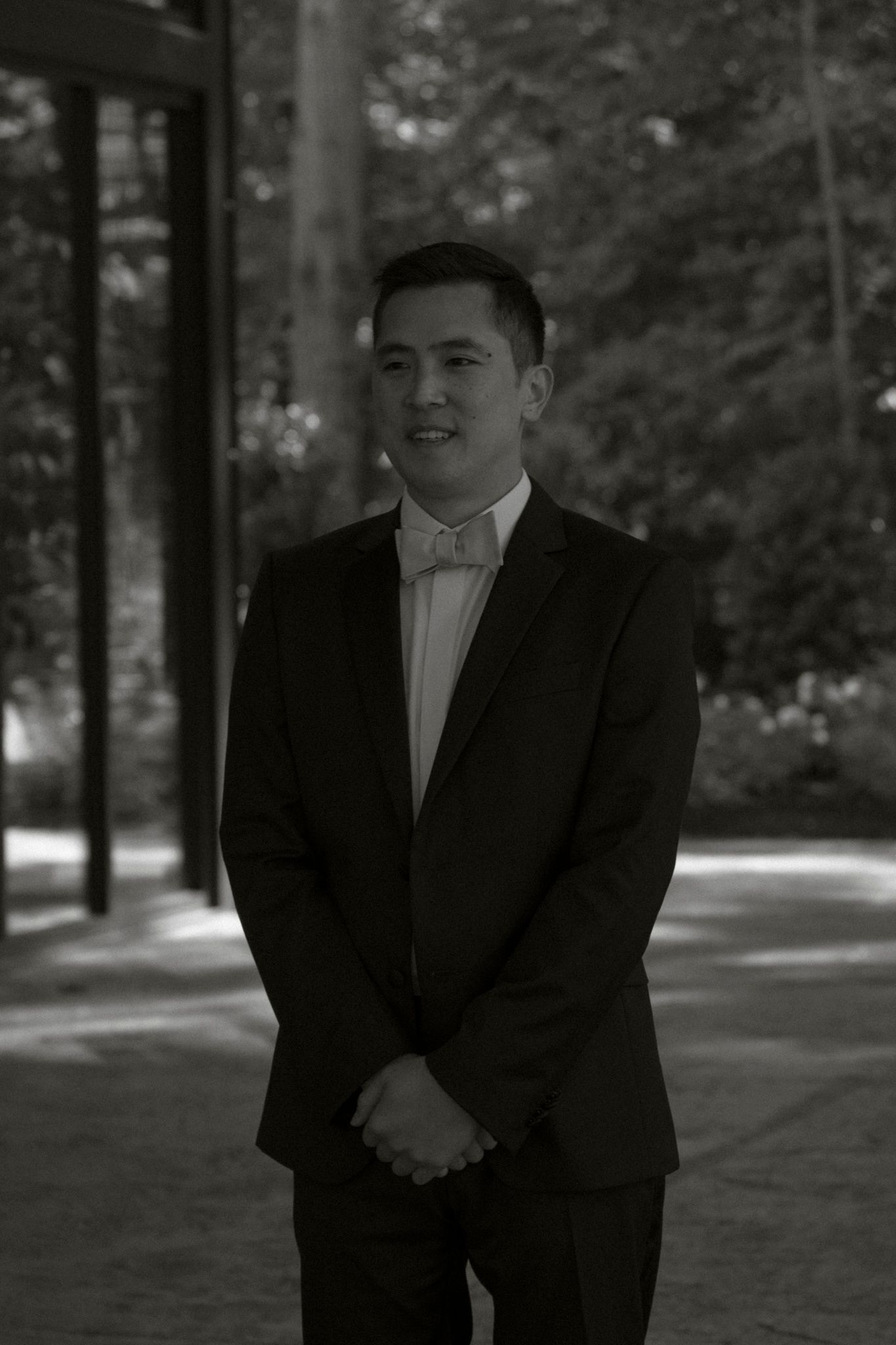 A series of black and white photos showing someone in a tuxedo smiling and posing in a wooded outdoor setting.