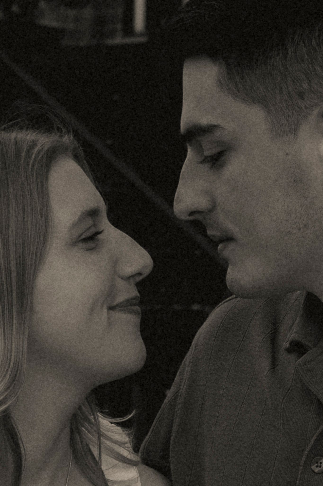 Black and white photo of a young couple gazing at each other intimately, captured in a romantic close-up portrait.