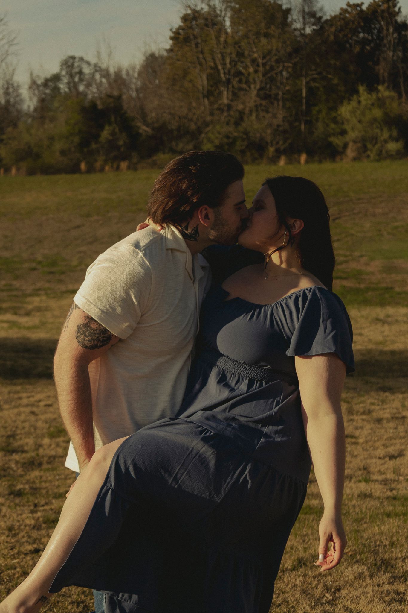 Couple sharing a romantic kiss outdoors in a sunny open field.
