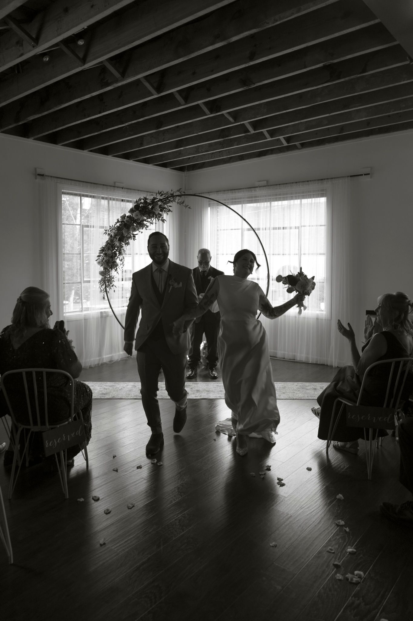 Silhouettes of people gathered in a minimalist room with exposed ceiling beams and large windows.