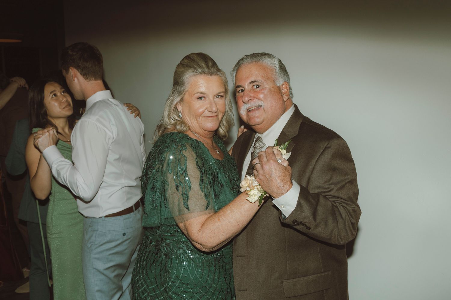 Couples dancing together at a formal event in elegant attire with green and brown color tones visible.