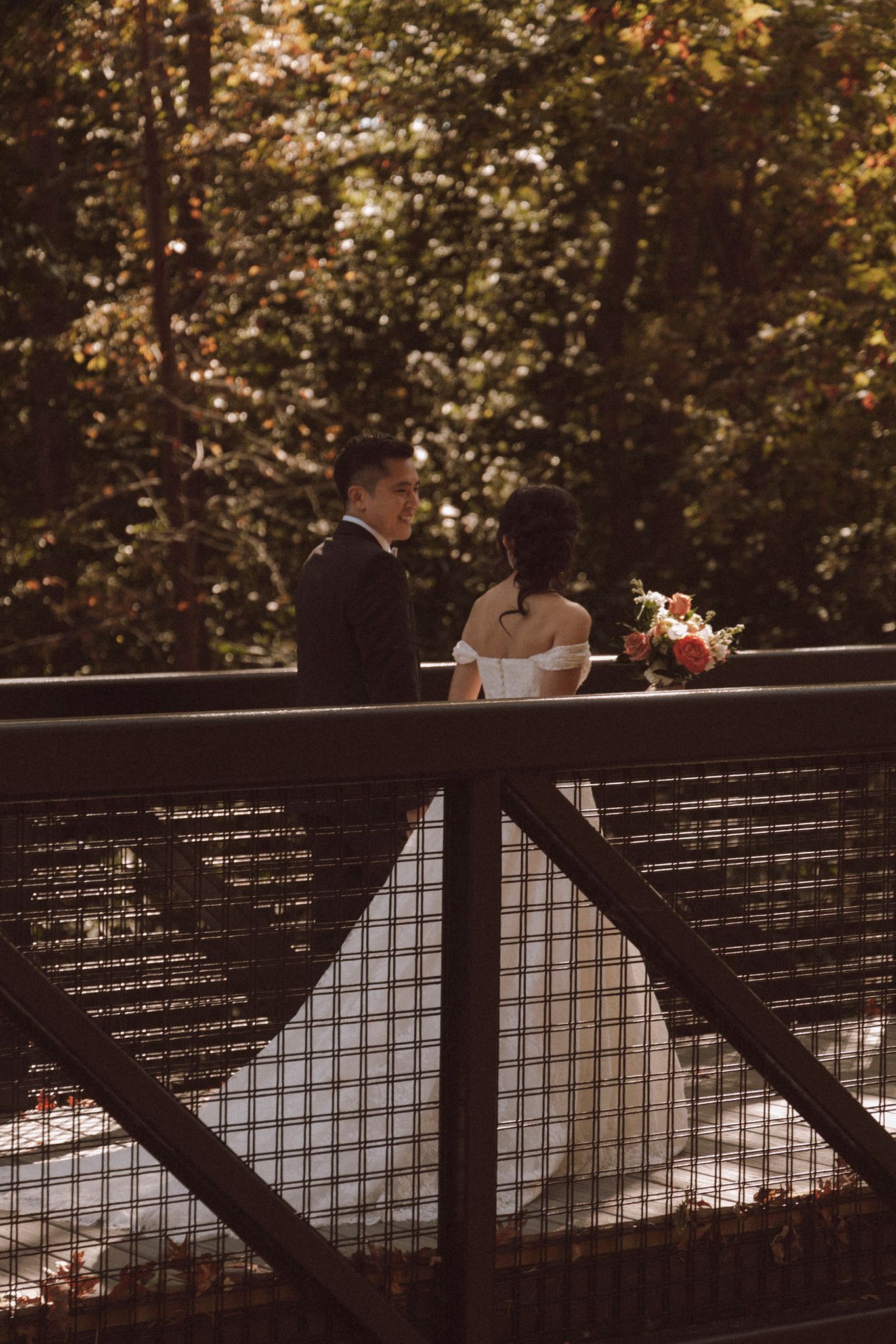 Silhouetted couple sharing a romantic moment on a bridge railing at sunset with trees in background.