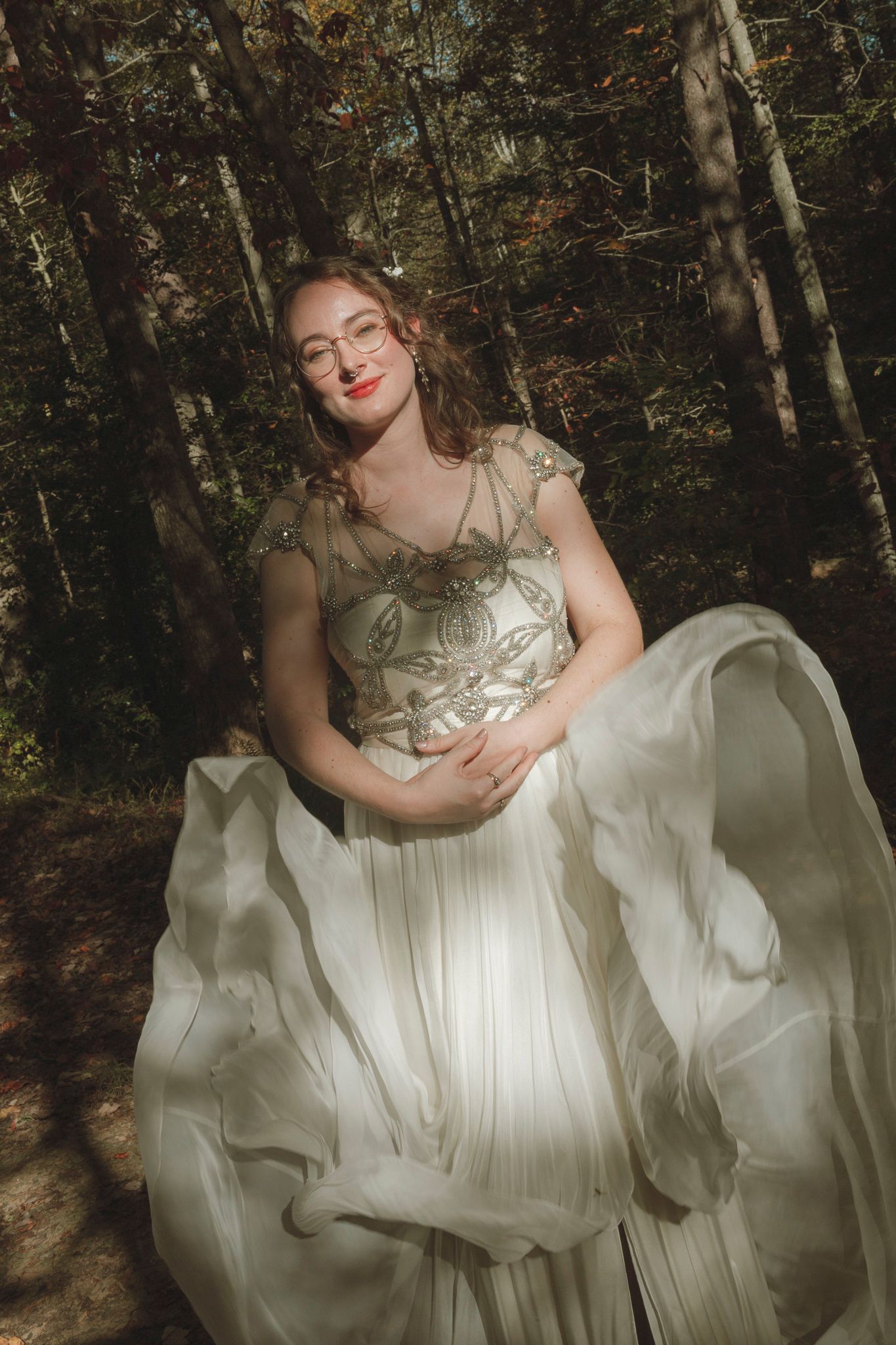 Ethereal white wedding dress flows in woodland setting with soft autumn light filtering through trees.