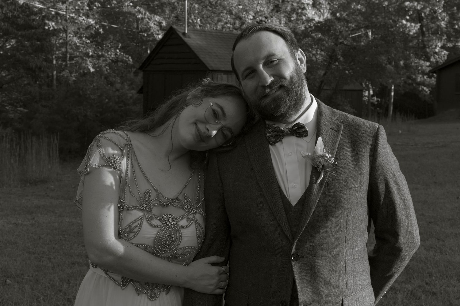 A couple embraces and smiles together in an outdoor setting with trees in the background.