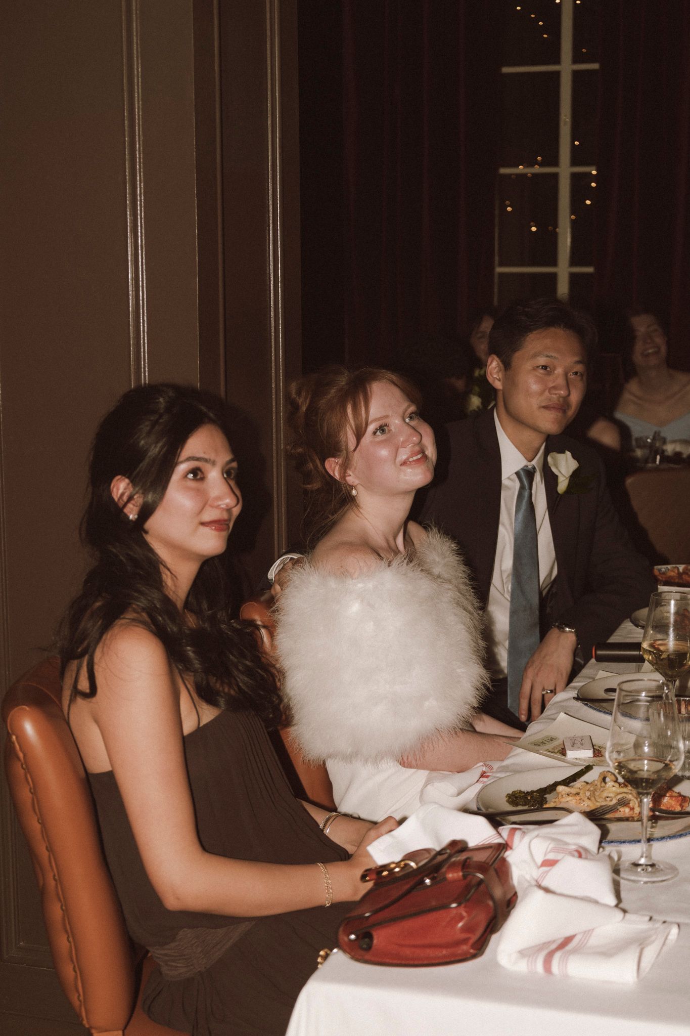 Three wedding guests seated at a dining table during a formal reception dinner in an elegant restaurant.