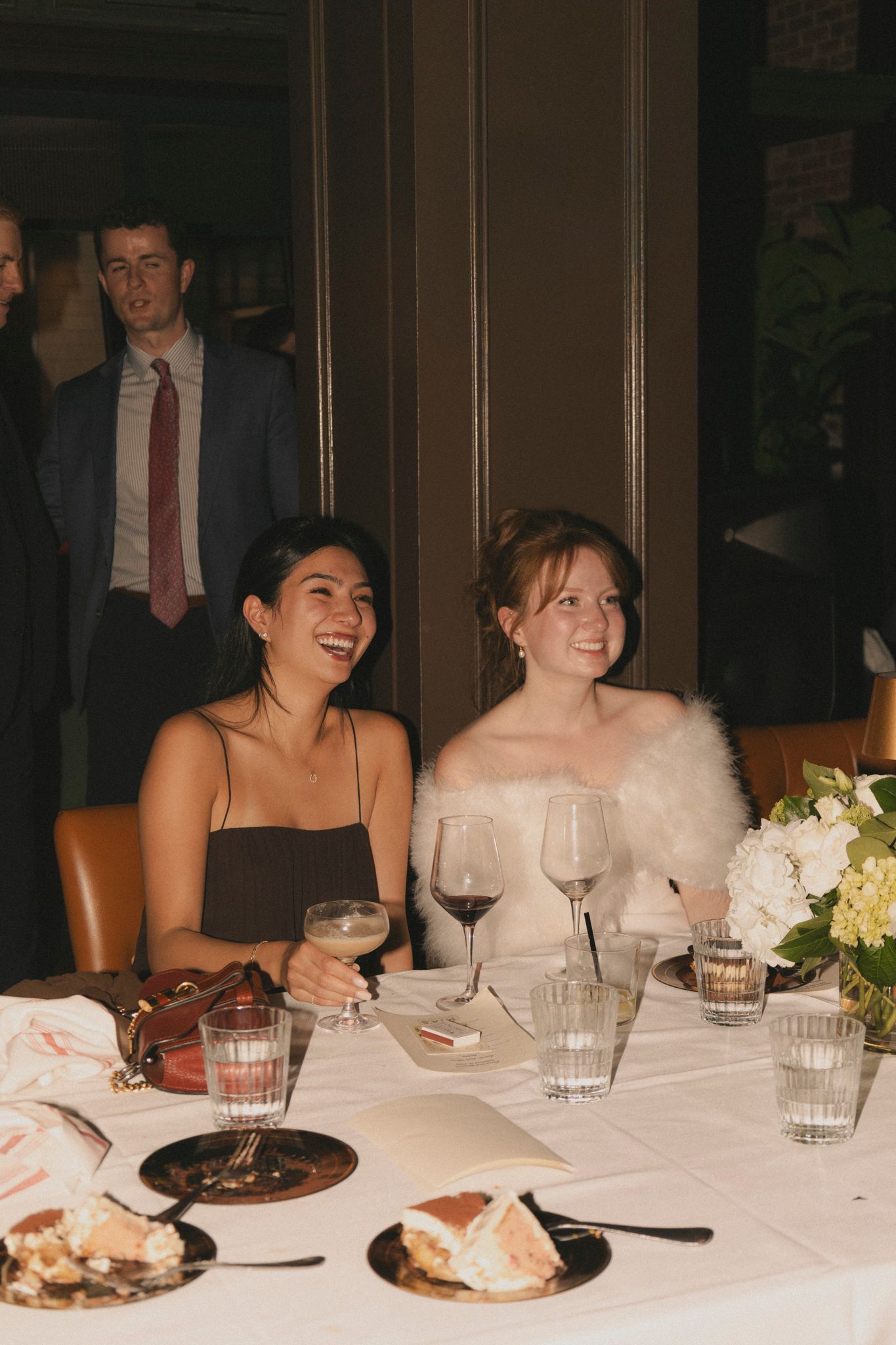 Bride in off-shoulder gown with fur wrap smiling at wedding reception dinner table.