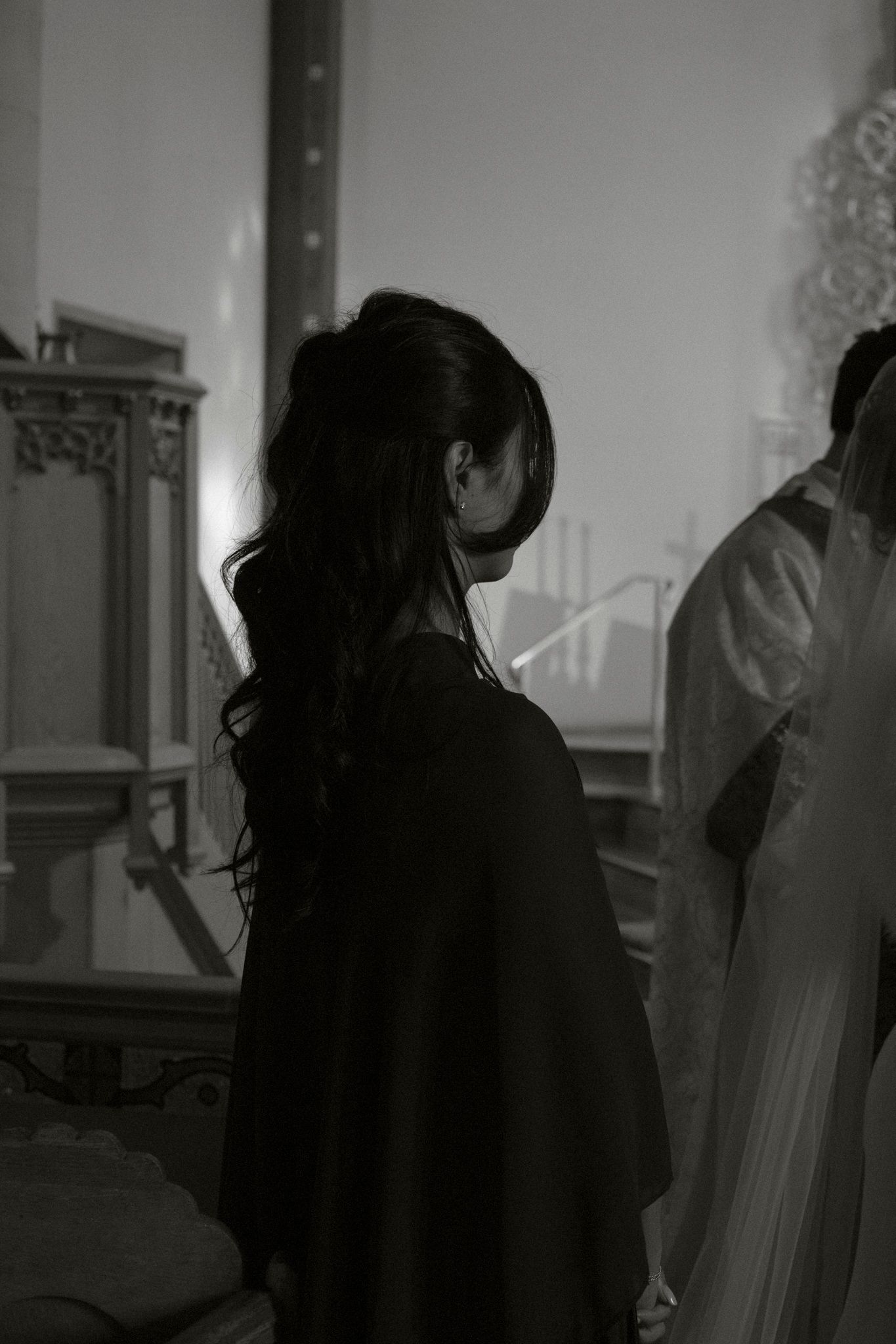 A woman in a black dress stands near a wedding altar in a black and white photo.